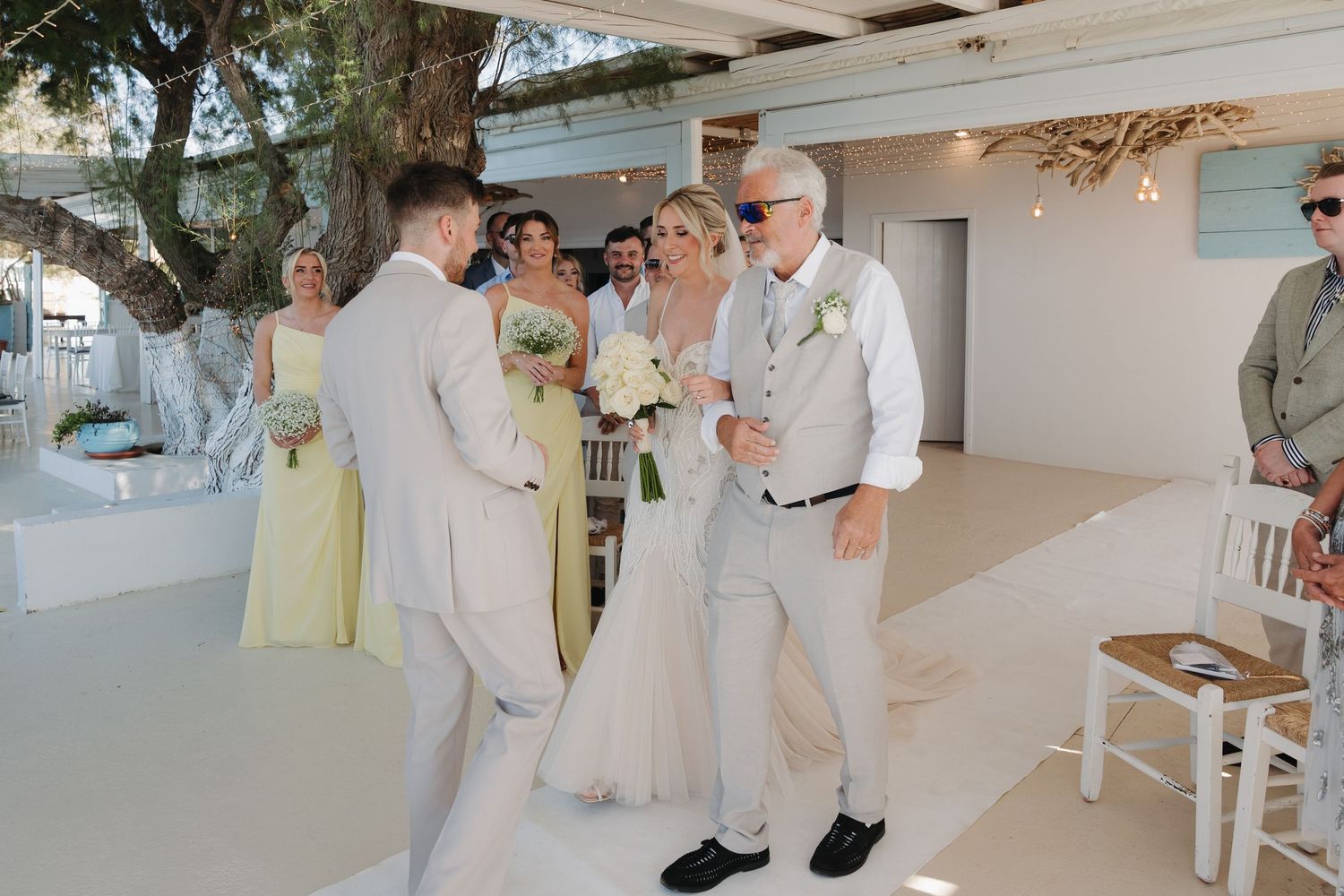 Wedding celebration on a bright coastal terrace with guests in light summer attire.