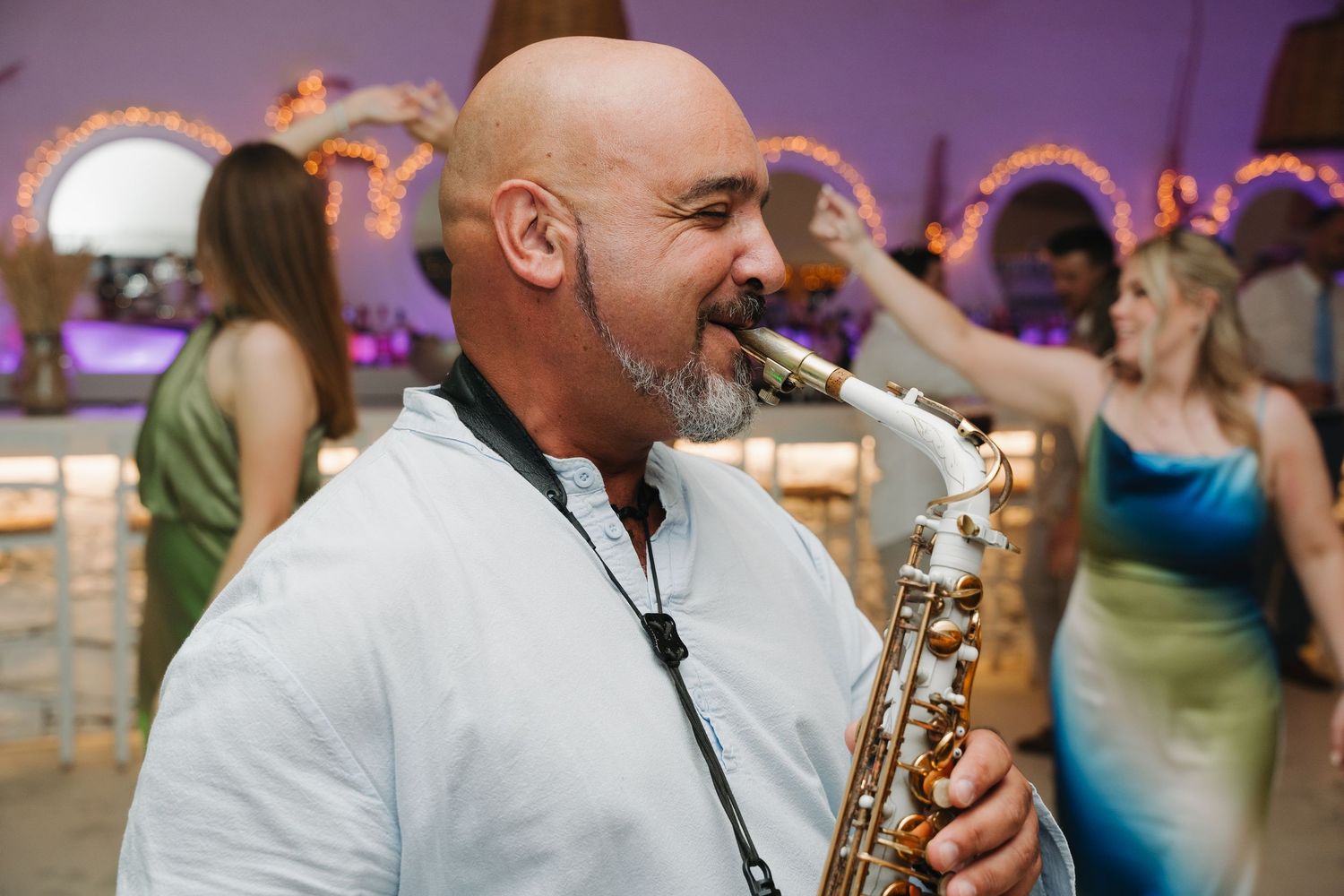 A saxophone player performs energetically at a wedding reception with party lights in background.
