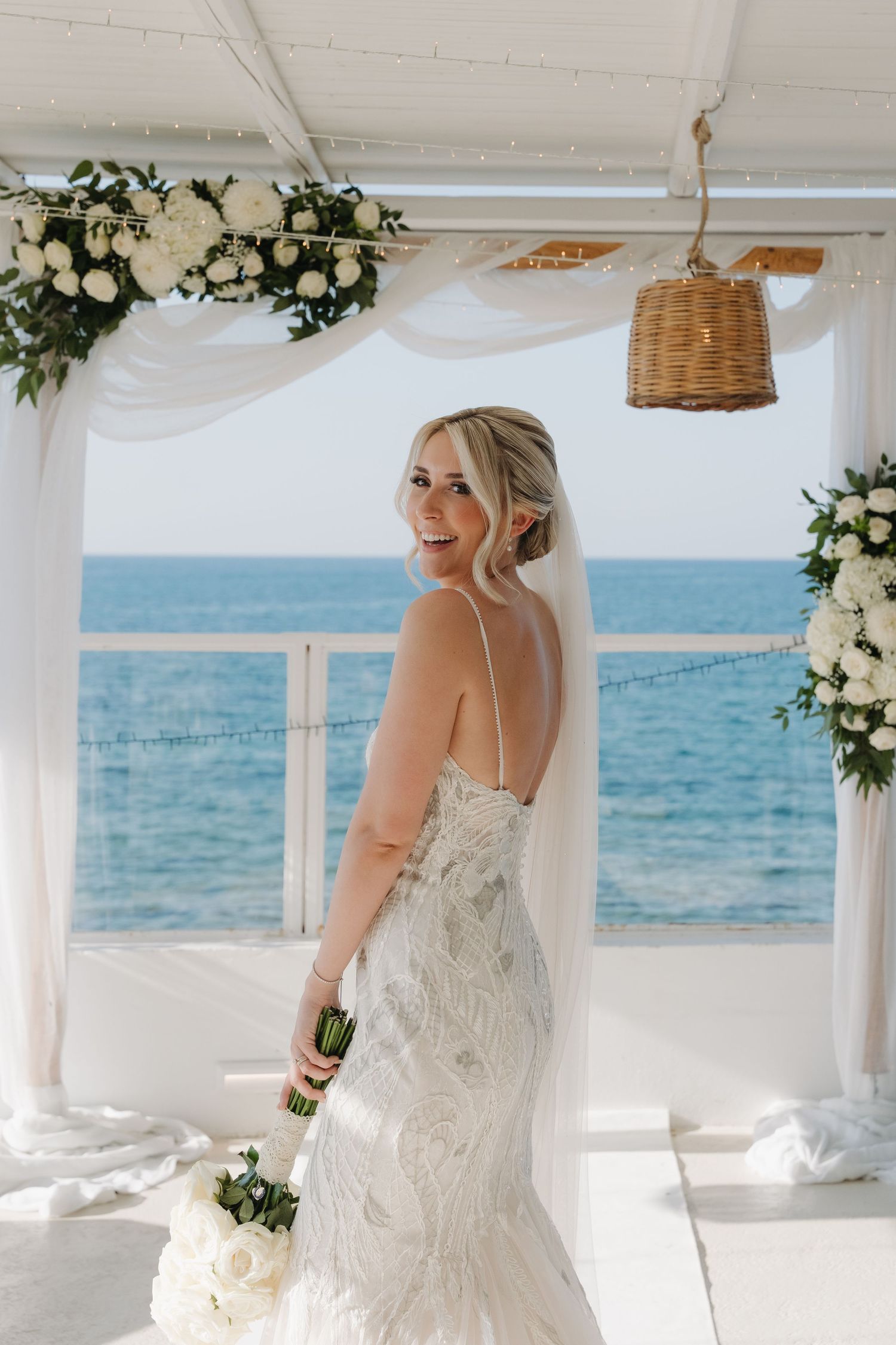 Coastal wedding ceremony setup with white floral arch and ocean view backdrop.