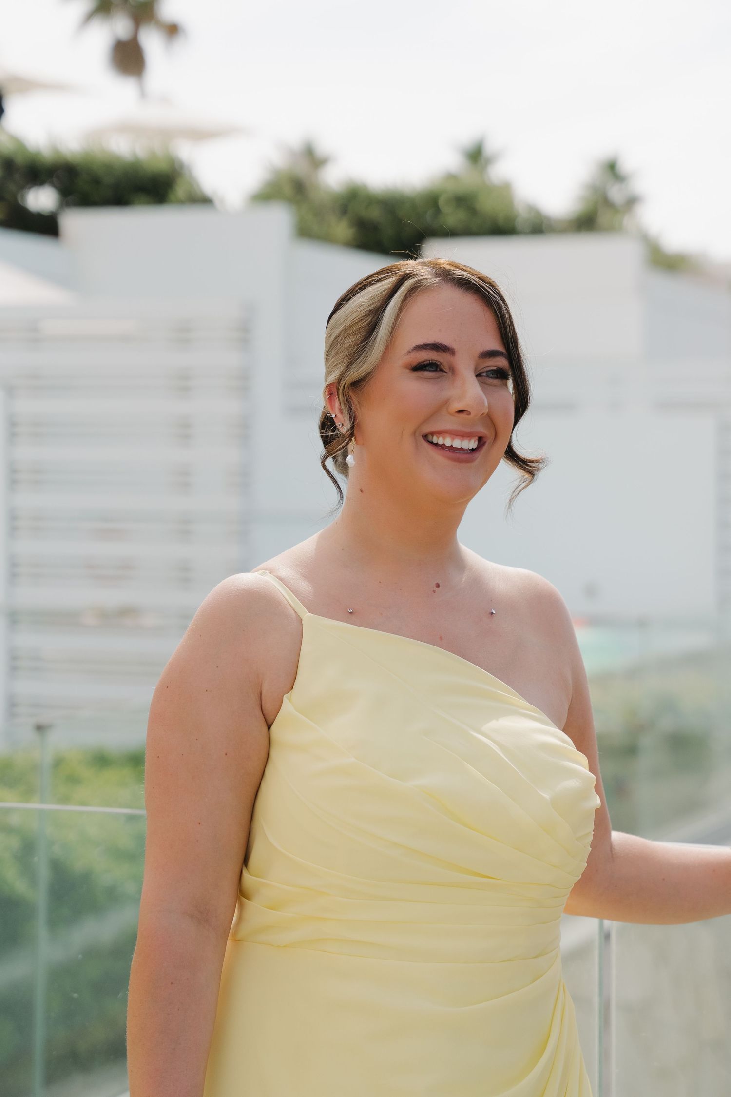 Bridesmaid wearing strapless pale yellow gown smiles during outdoor wedding celebration.