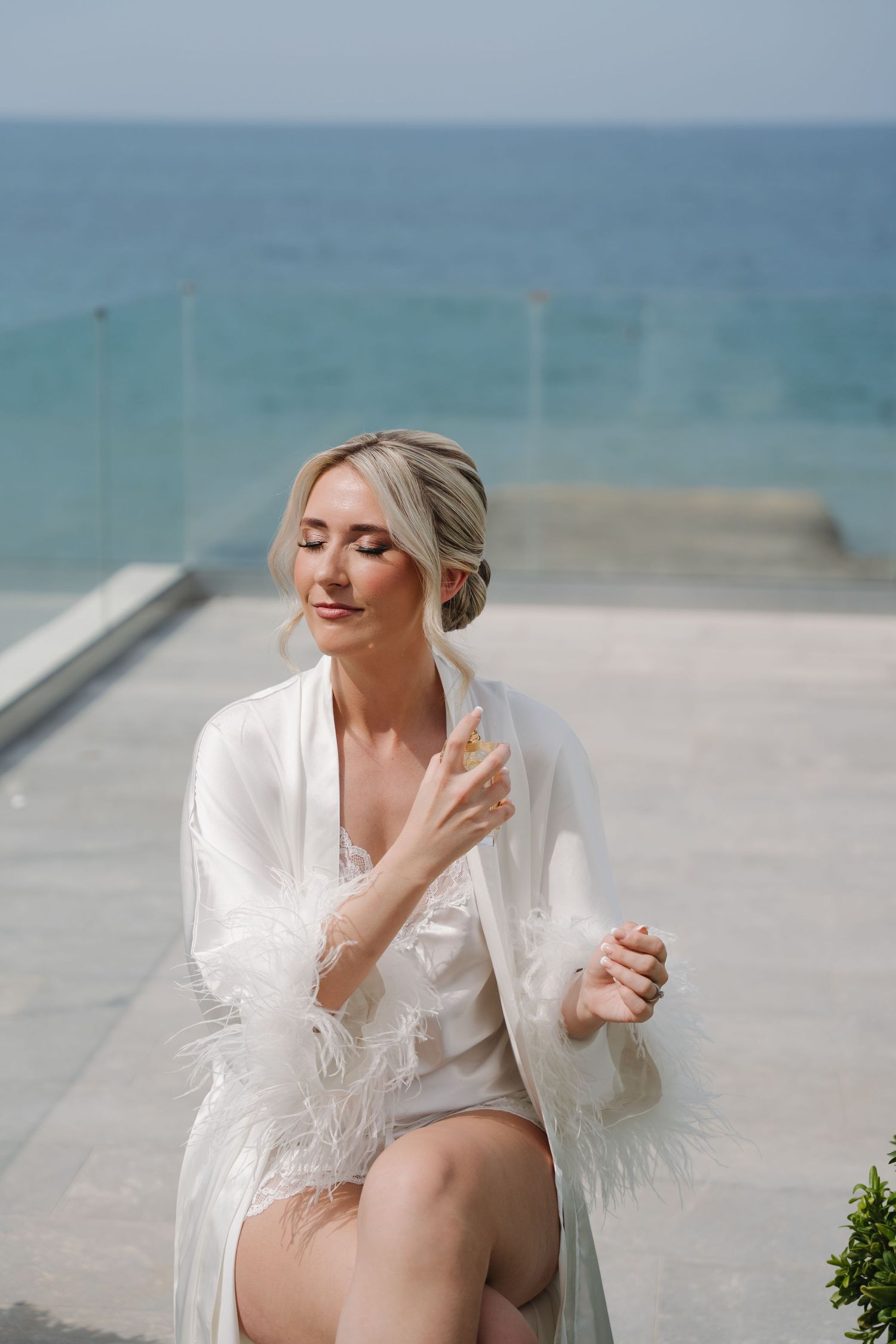 Seaside bridal portrait featuring a white feathered robe against ocean backdrop.