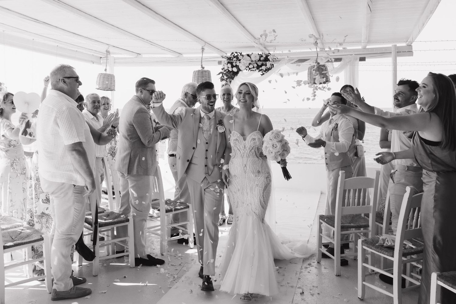 Celebration at an outdoor wedding reception with guests dancing under a white tent by the sea.