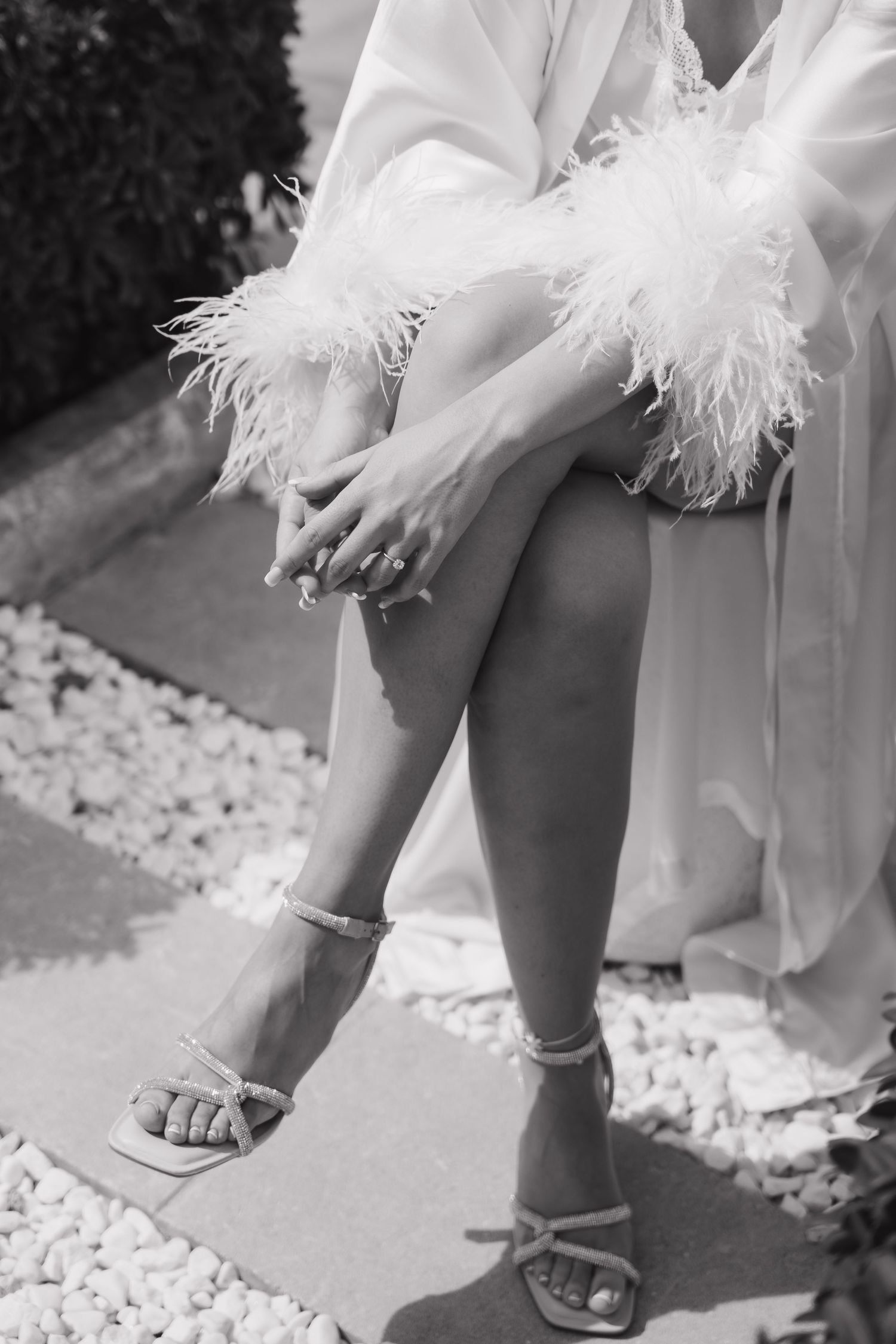Close up of bridal shoes and feathered robe hem on light gravel pathway.