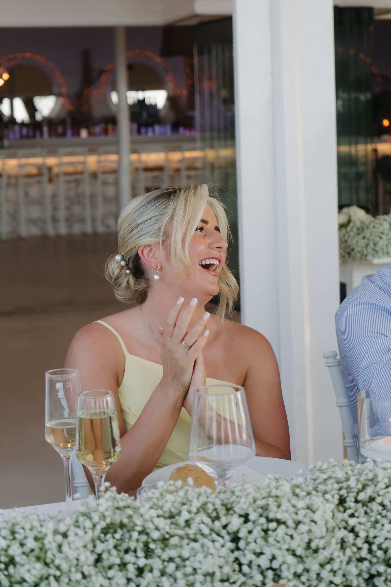 Reception guest laughs while seated at table decorated with delicate white flowers.