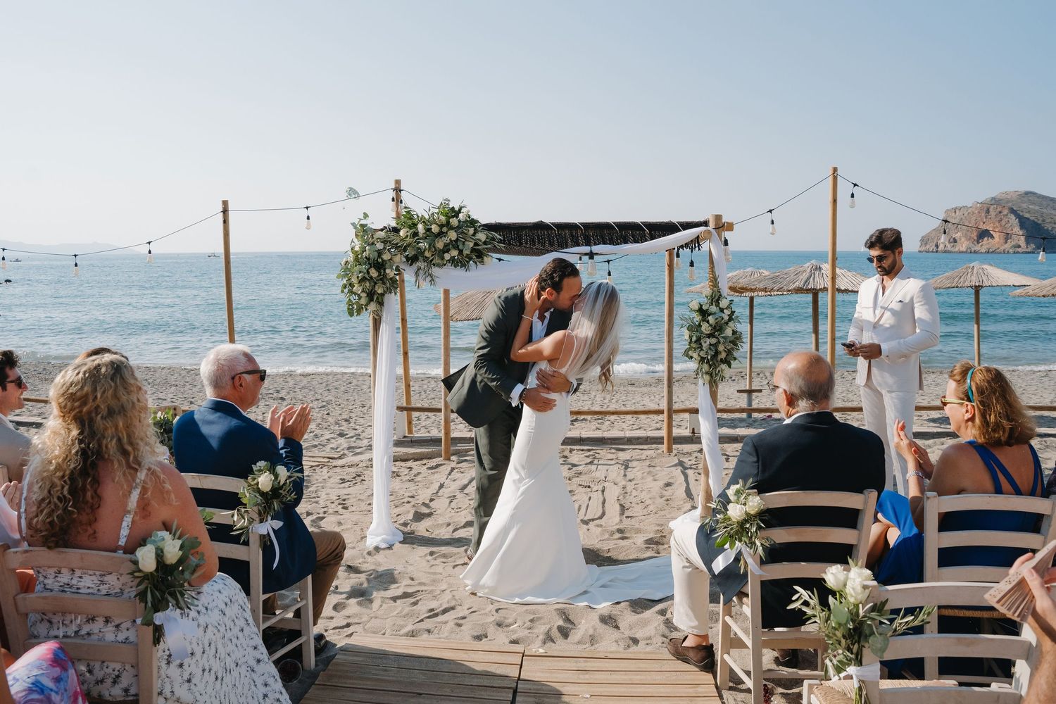 Wedding guests seated at a beachfront ceremony with string lights and ocean views.