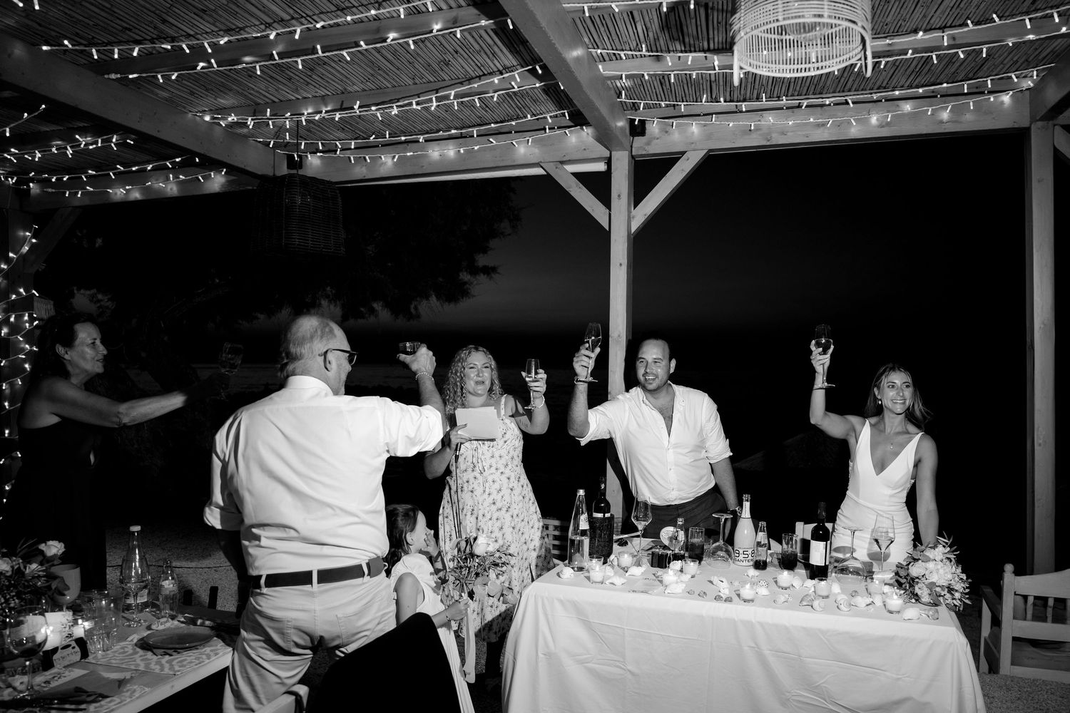 Wedding reception guests celebrating and dancing under string lights at an outdoor venue.