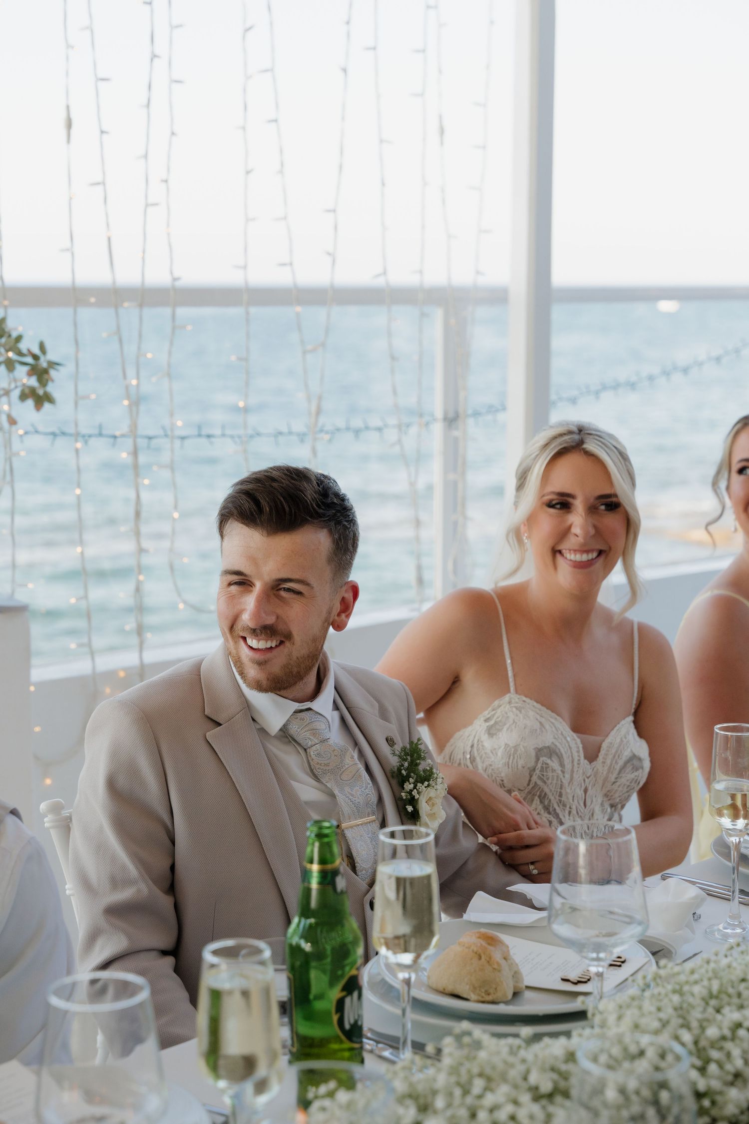 Wedding reception table setting with ocean view backdrop and string lights creating romantic atmosphere.
