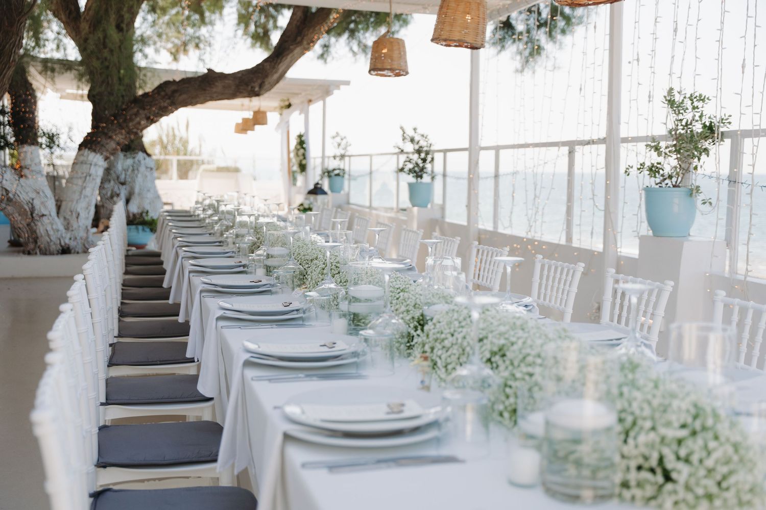 Long wedding reception table decorated with baby's breath centerpieces and white chairs overlooking the ocean.