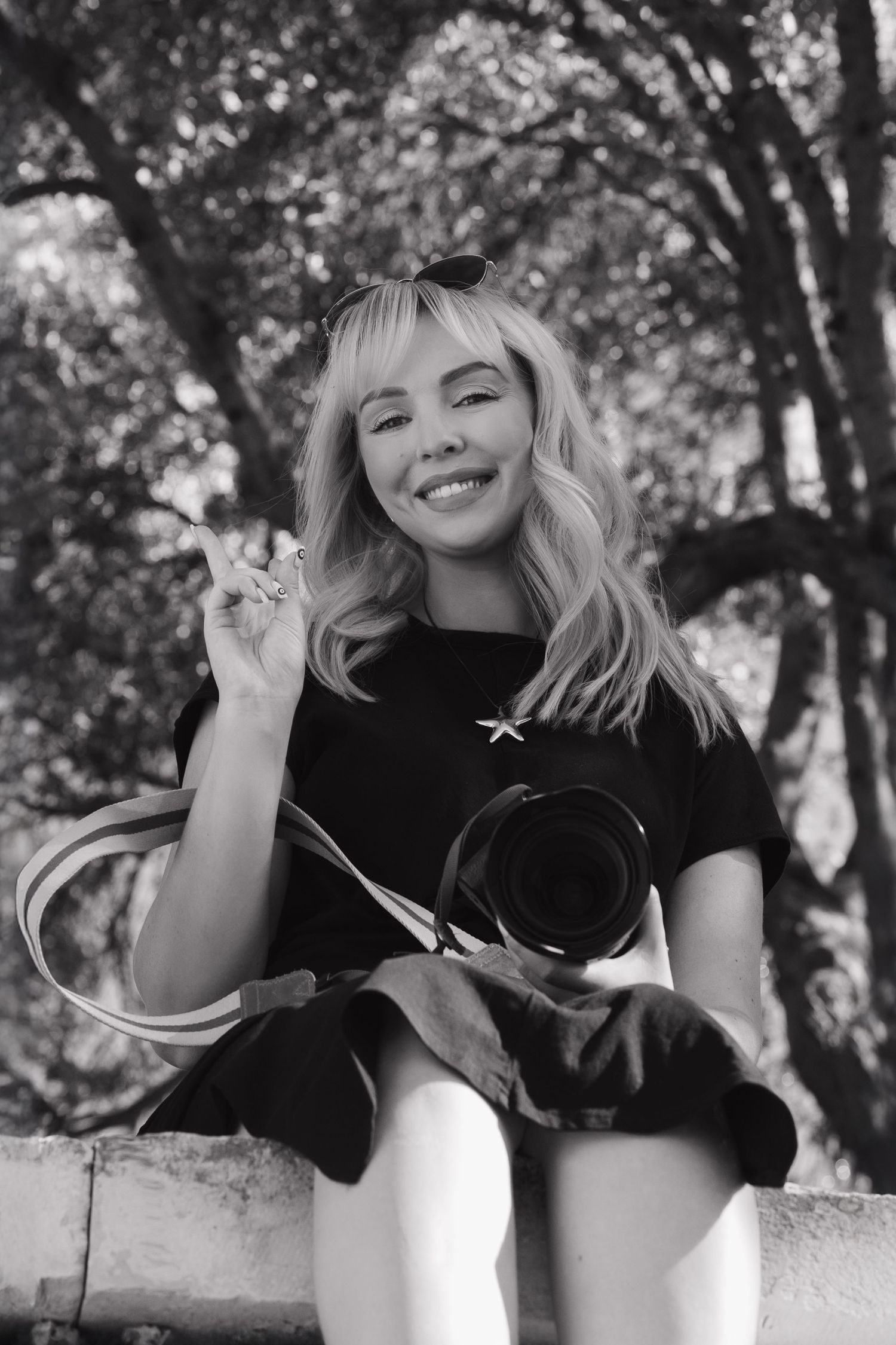 Black and white portrait of a photographer holding a camera outdoors in a natural setting.
