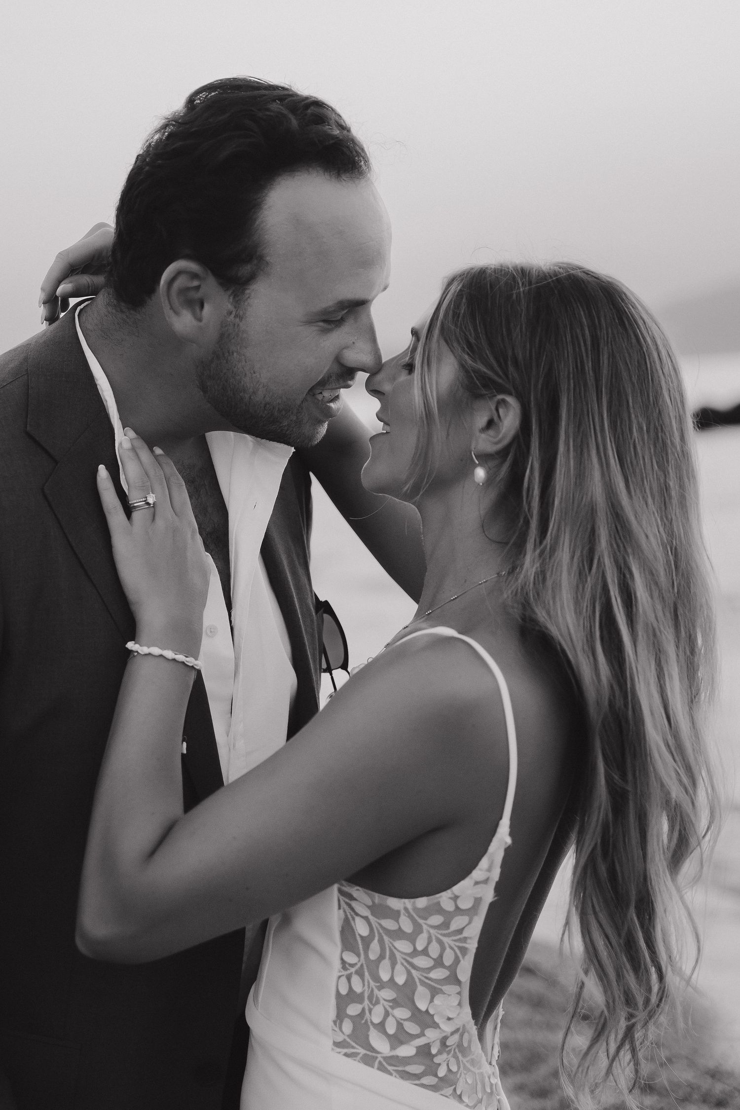 An intimate black and white wedding portrait of a couple sharing a tender moment by the water.