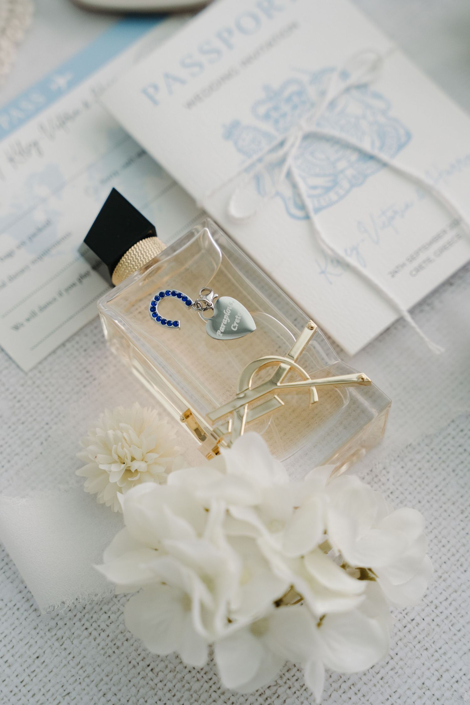 Elegant perfume bottle and white flowers arranged with passport on linen surface.