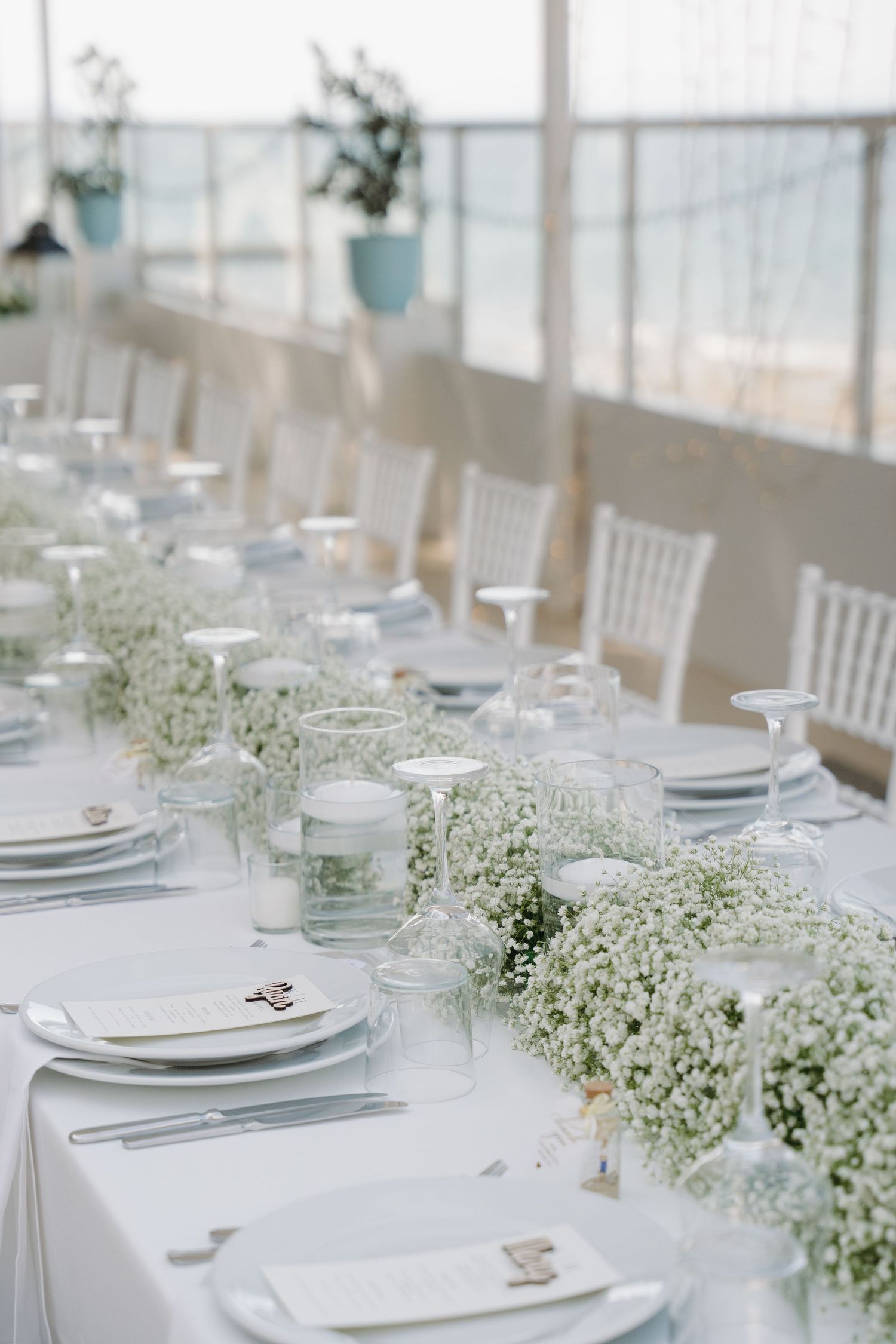 Elegant wedding reception table with white floral runner and place settings overlooking the ocean.