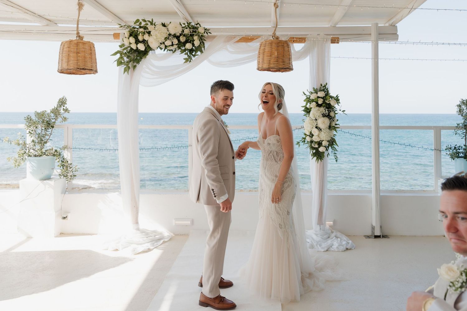 Beachfront wedding ceremony space with woven pendant lights and white floral arrangements.