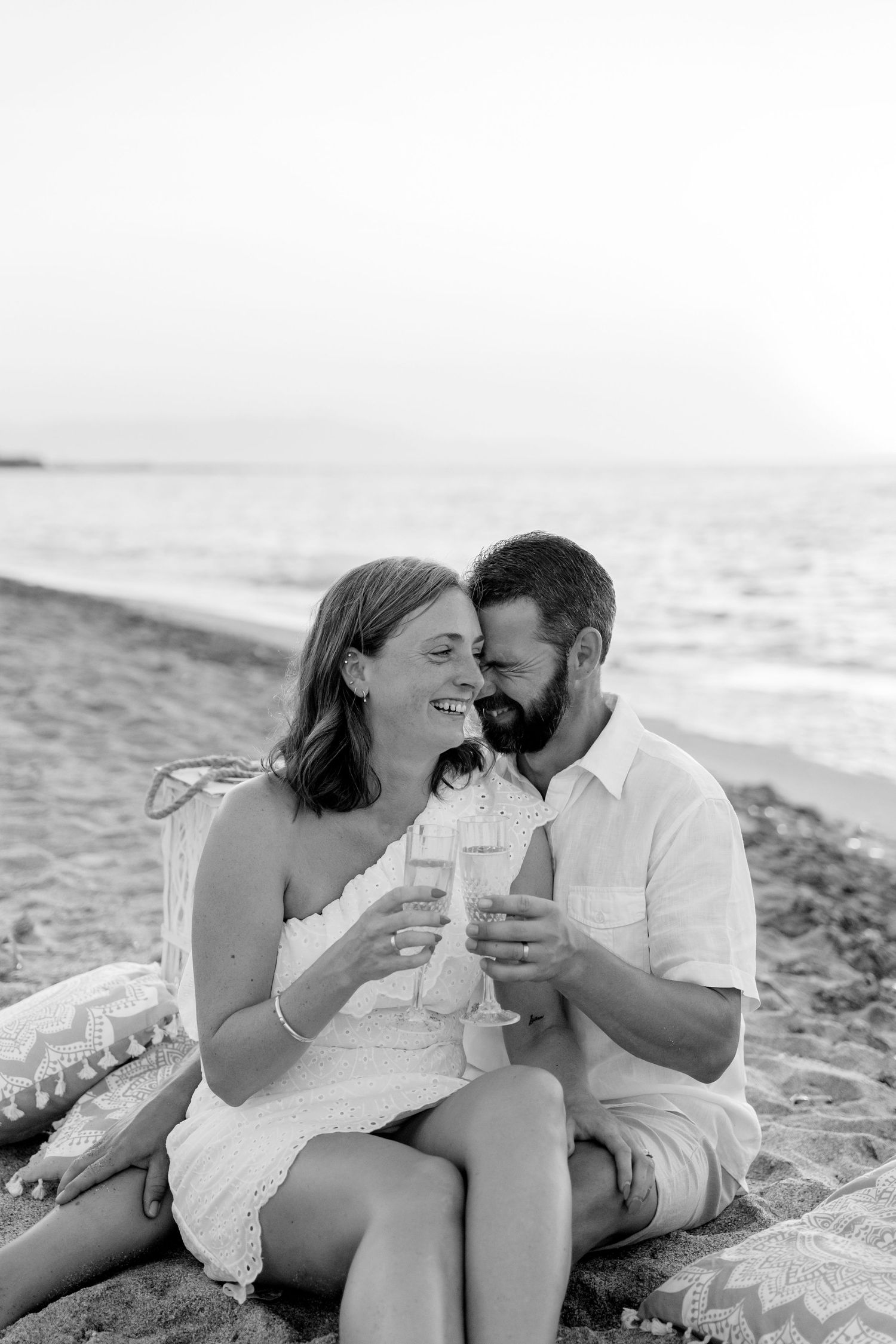 Black and white portrait of couple sharing drinks on beach blanket.