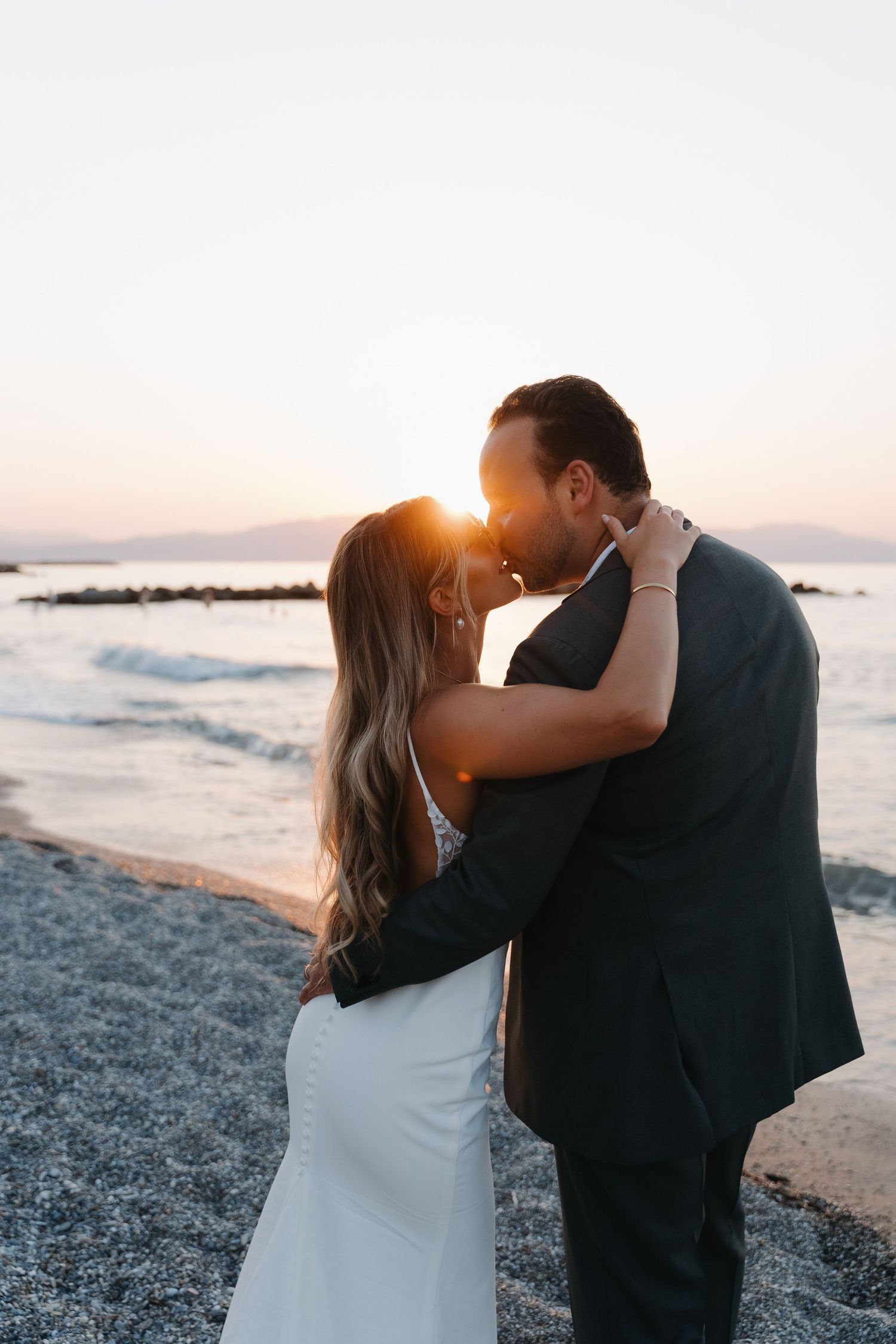 A couple shares a romantic sunset kiss on the beach during their wedding day.