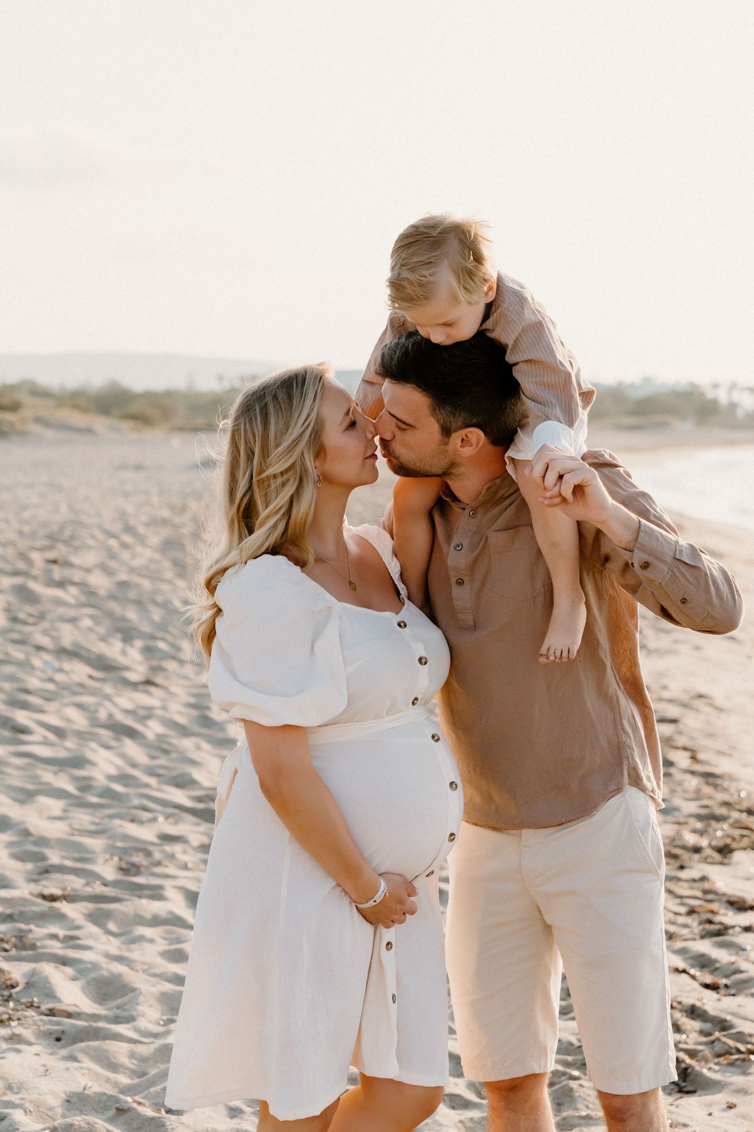 Family shares intimate moment on beach during sunset maternity photoshoot.
