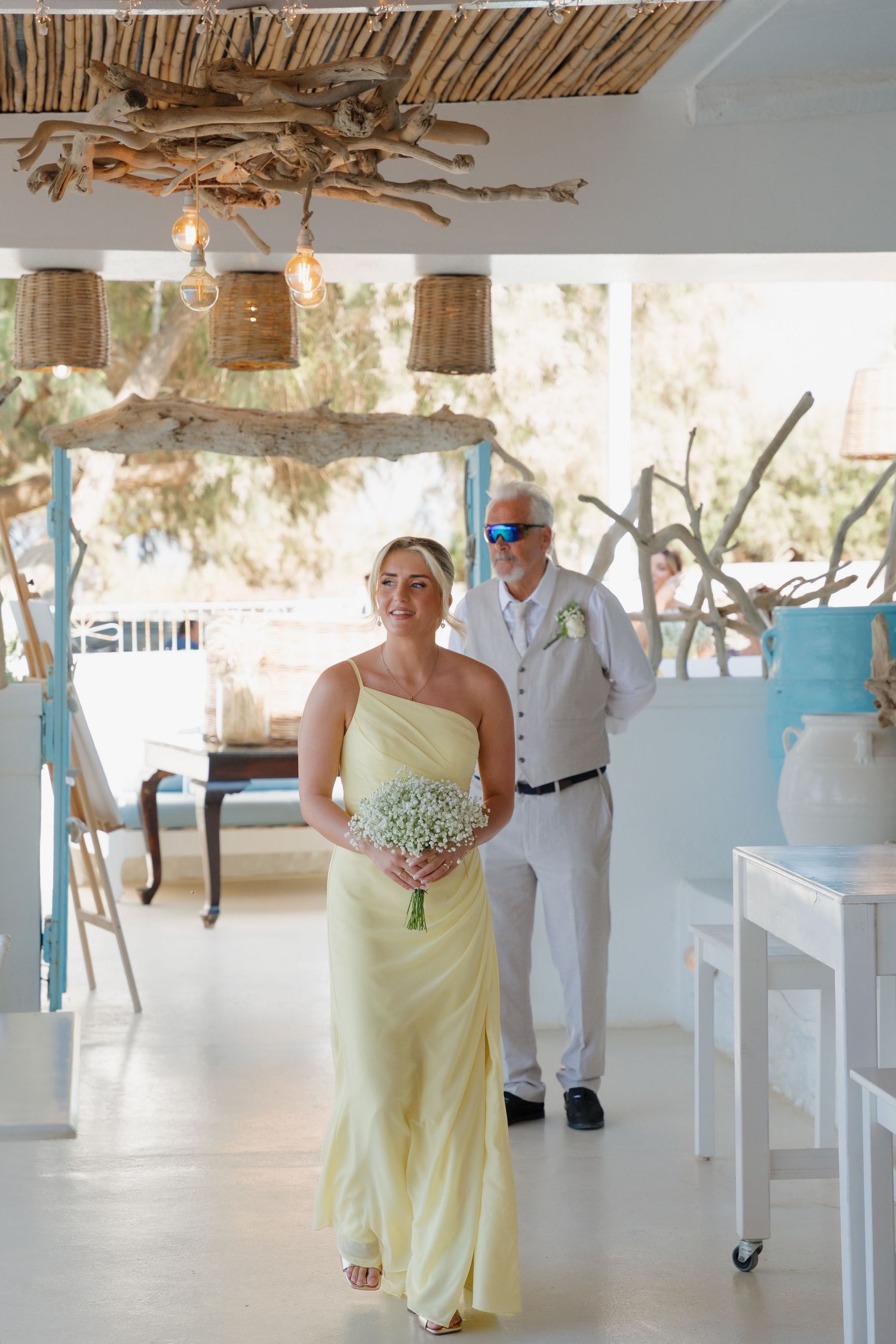 Attendant in pale yellow dress walks down aisle at beach wedding venue.
