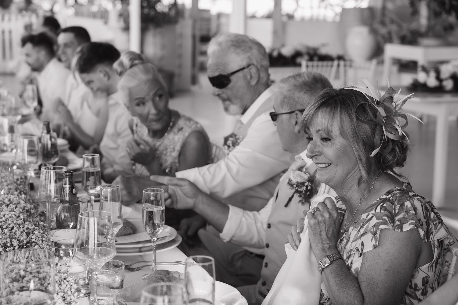 Black and white candid photo of wedding guests enjoying dinner at outdoor reception.
