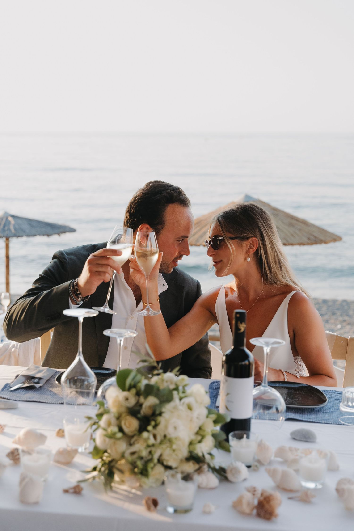 Romantic beachside dinner with wine glasses and floral centerpiece.