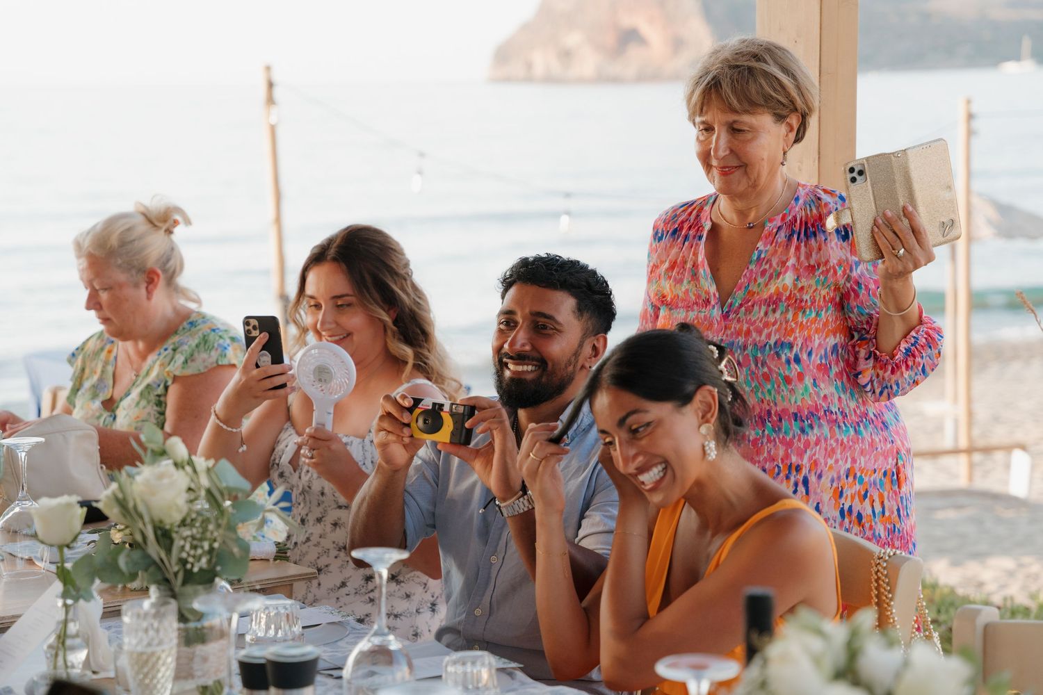 Wedding reception guests enjoying a celebration under covered outdoor seating area.