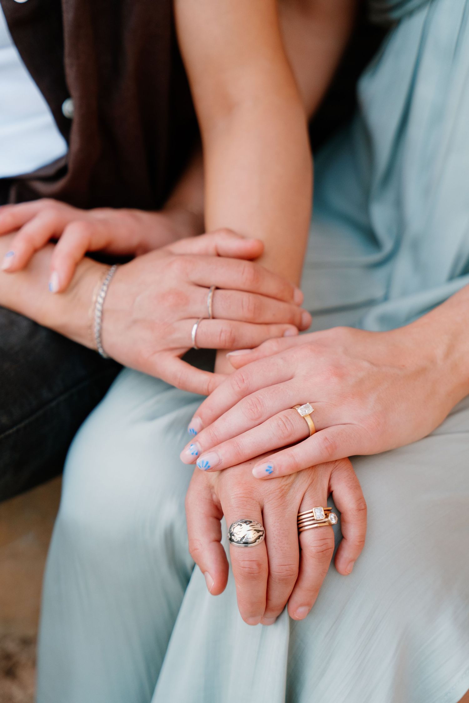 Close-up of hands with multiple rings and bracelets resting on a light blue dress fabric in Rethymno, Crete