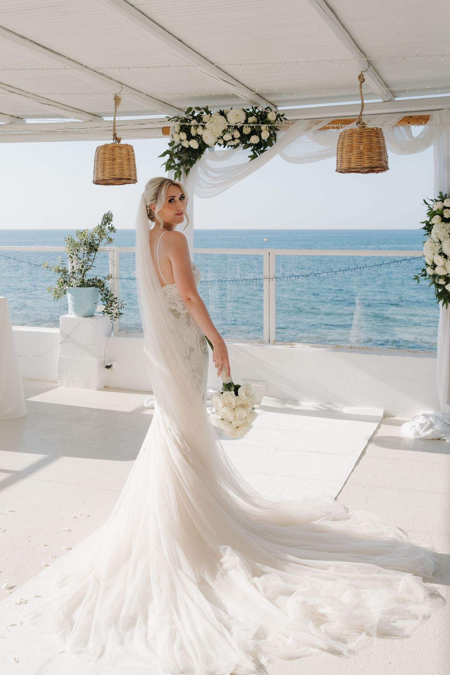 Elegant bridal portrait on a white terrace overlooking the ocean with wicker pendant lighting.