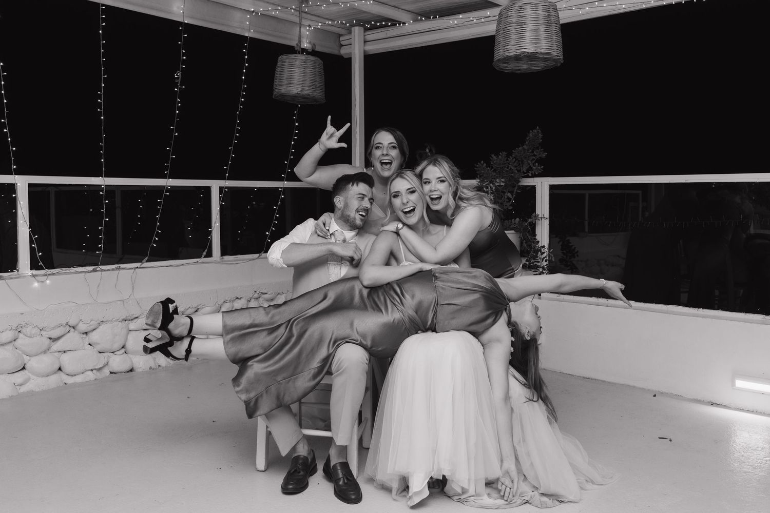 Wedding party members pose playfully together for a fun group photo at a waterfront venue.