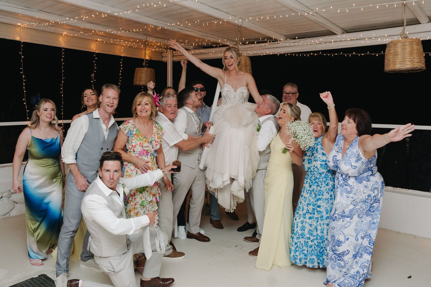 Wedding party celebrating with the newlyweds on a decorated outdoor terrace.