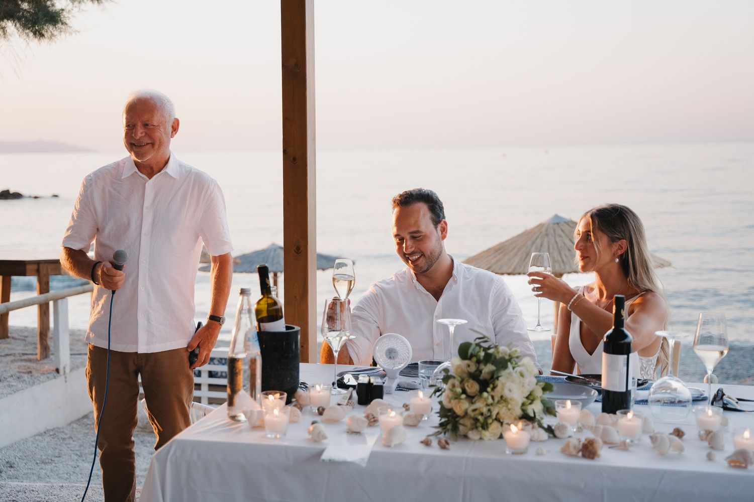 Elegant outdoor wedding reception dinner setup by the ocean at sunset.