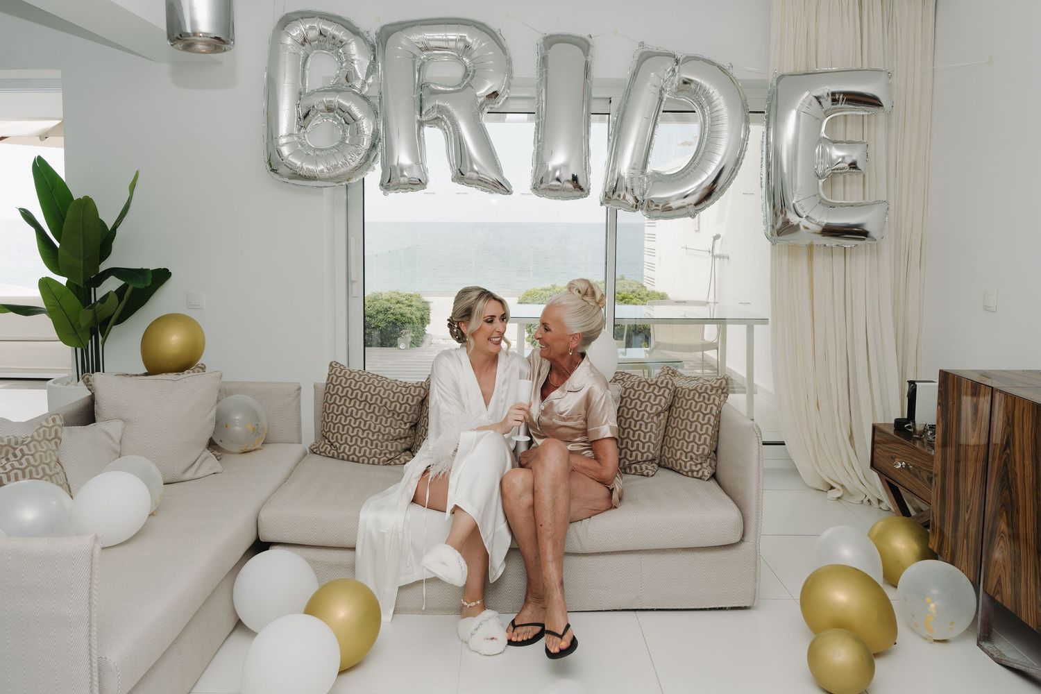 A decorated living room with silver BRIDE balloons, cream couch, and gold accents for a bridal celebration.