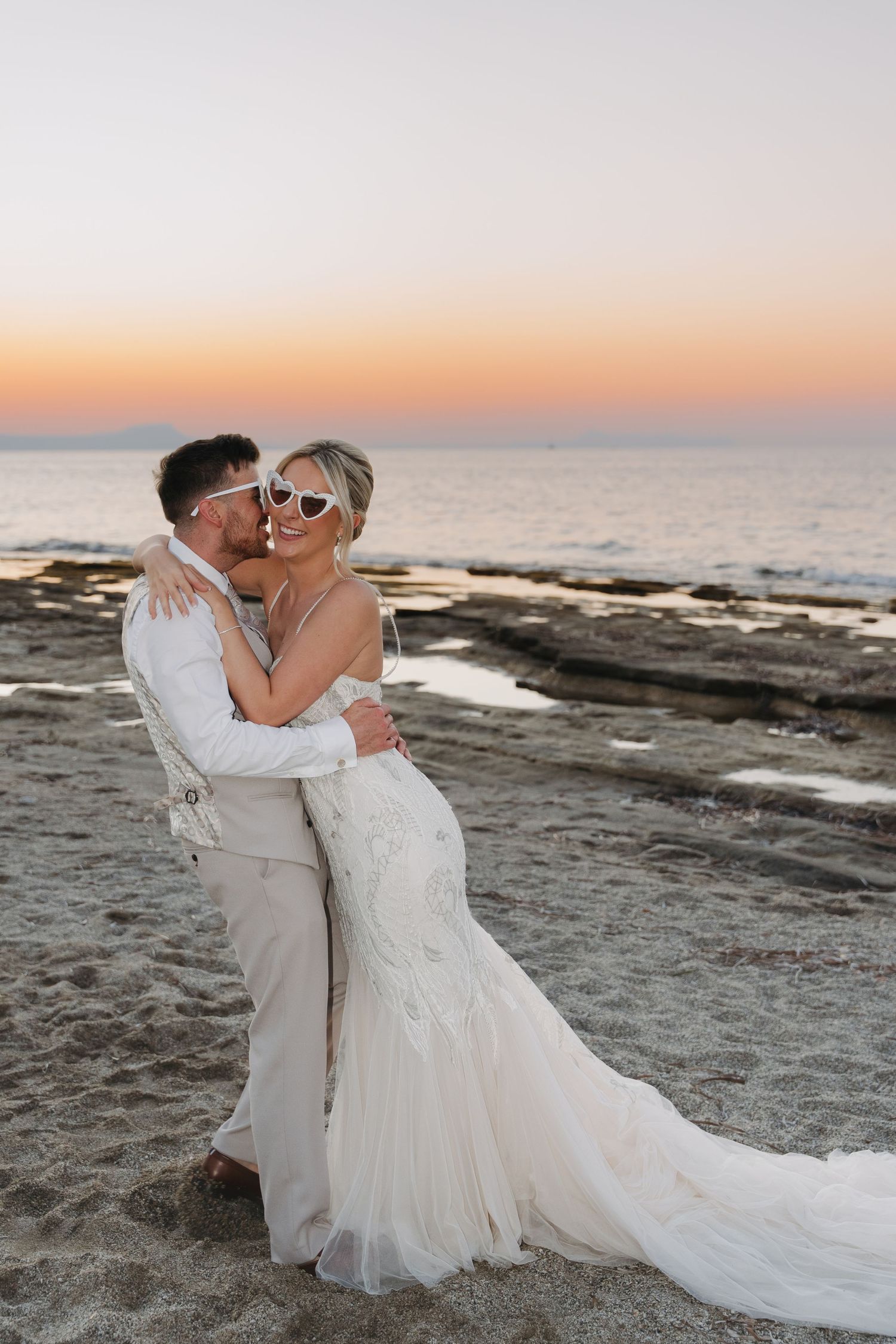 Intimate wedding couple moment at sunset on rocky beach with ocean backdrop.