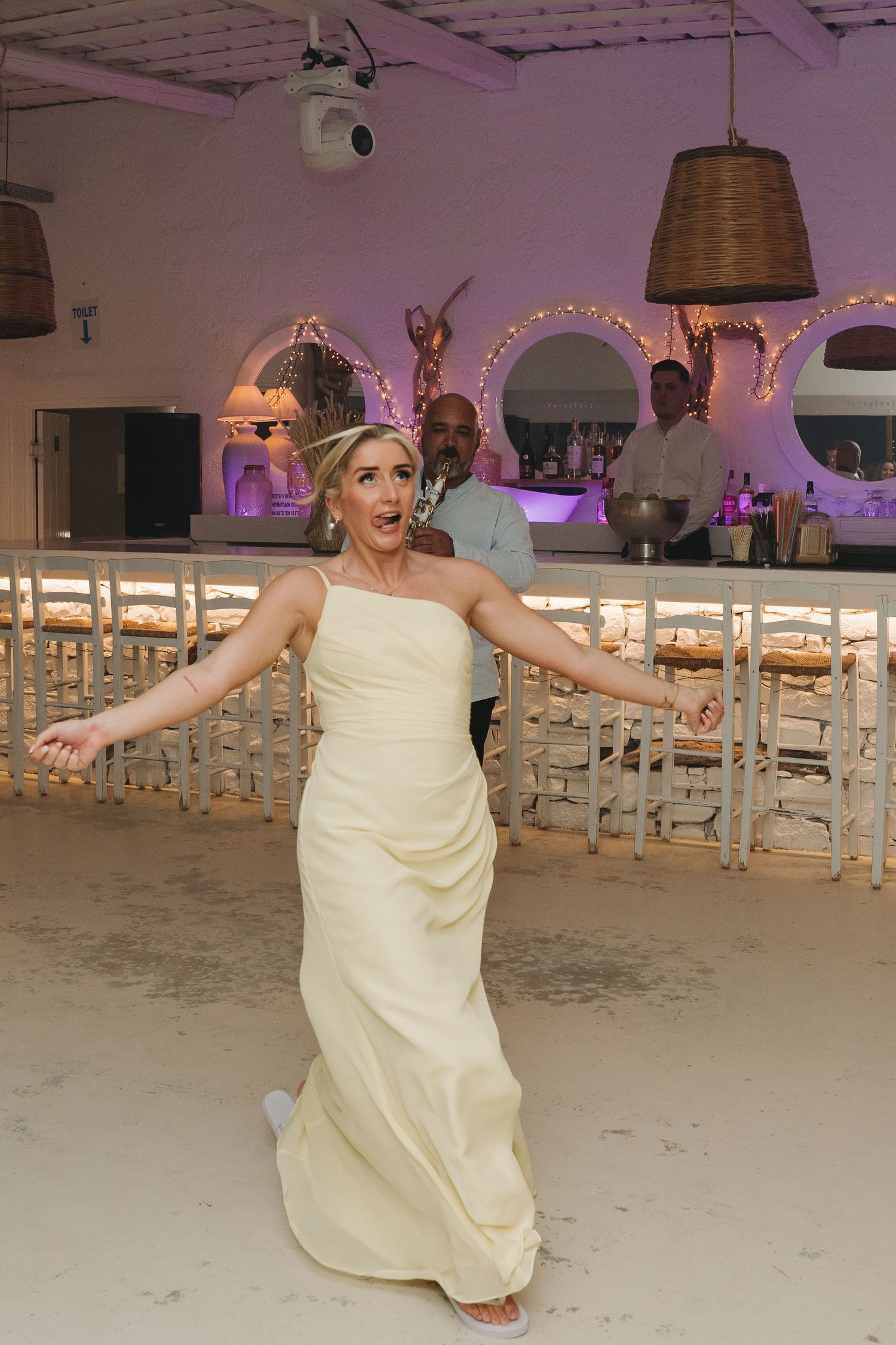 A guest dances joyfully in a cream-colored dress at a wedding reception with string lights.