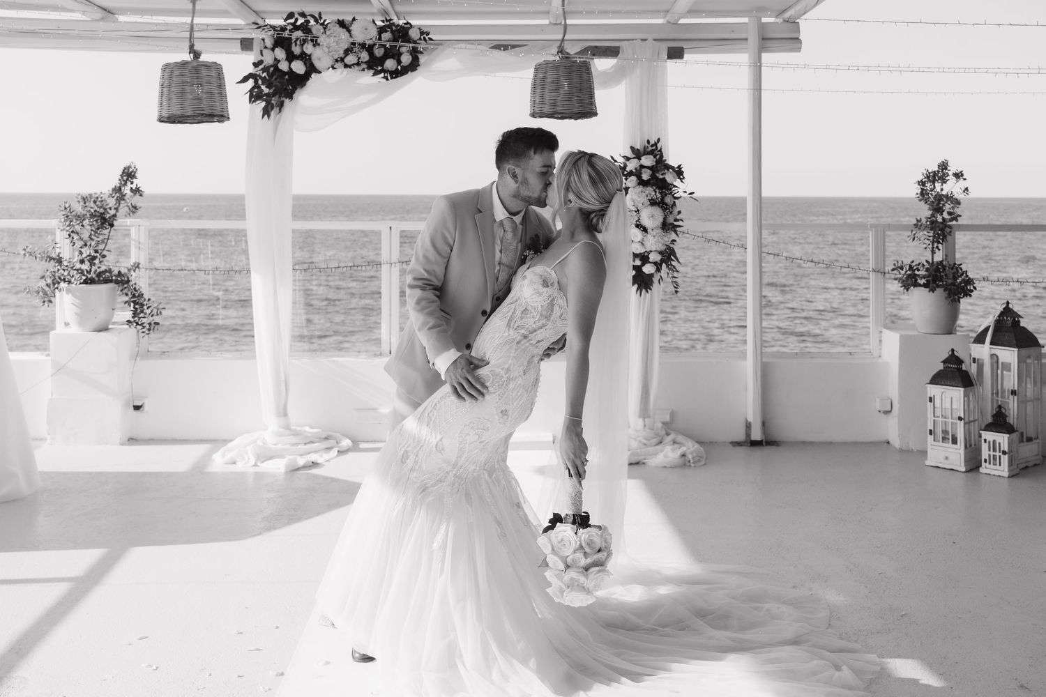 Romantic black and white wedding dance photo under decorated oceanfront pavilion.