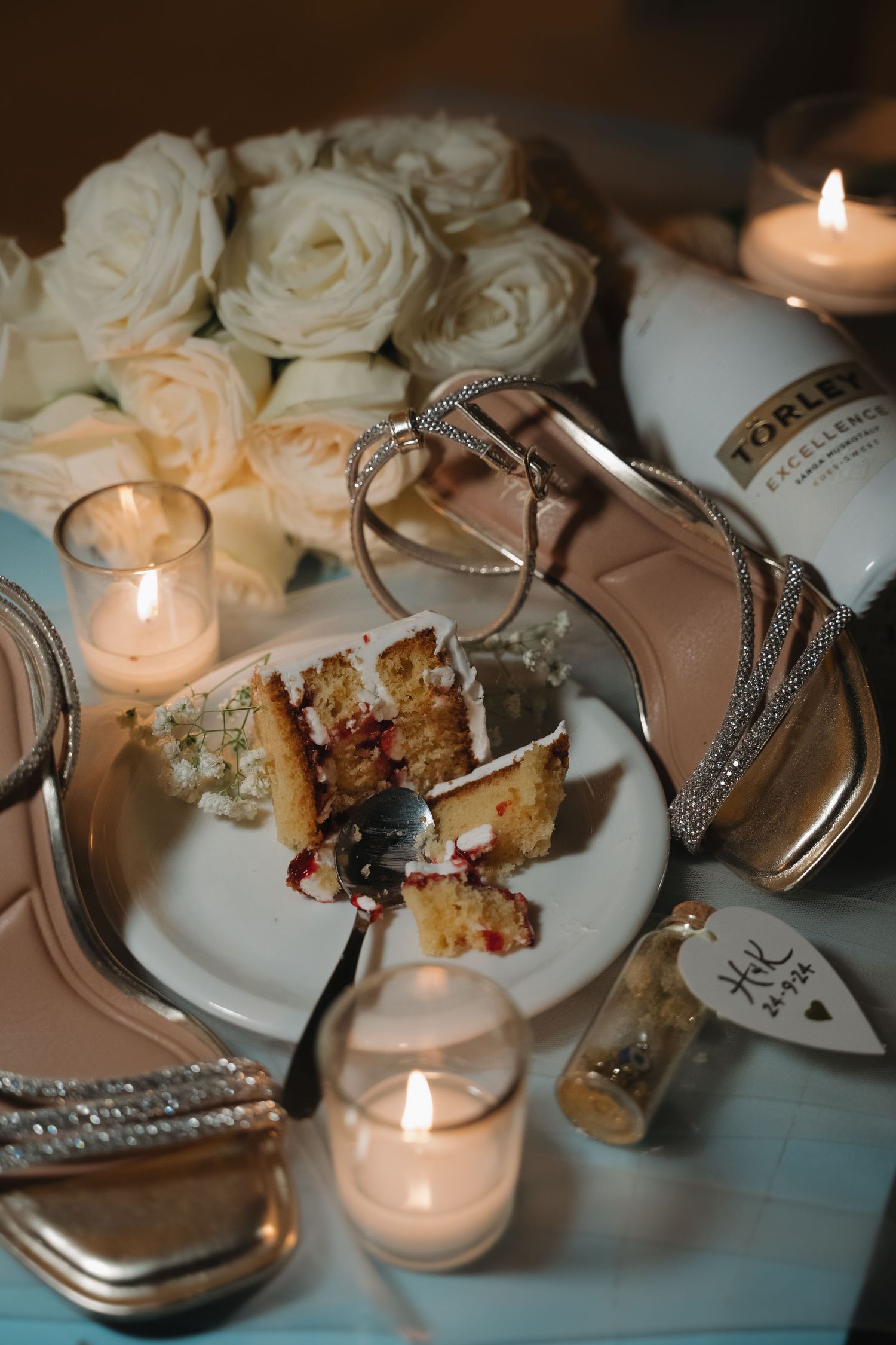 Wedding reception details with roses, candles, cake, and sparkly bridal shoes on an elegant table setting.