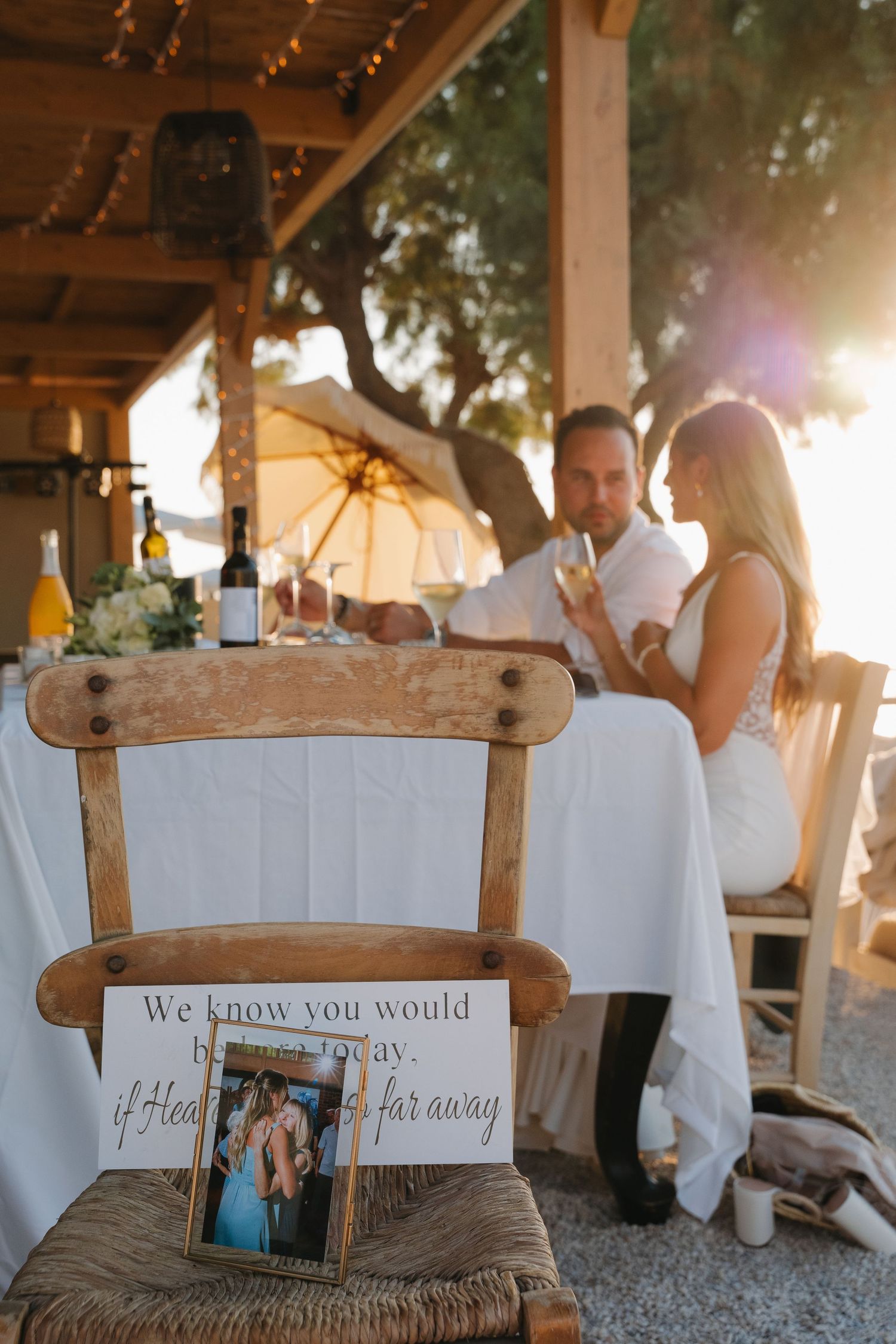 Wedding reception table with memorial chair and photo frame at sunset under wooden pergola.