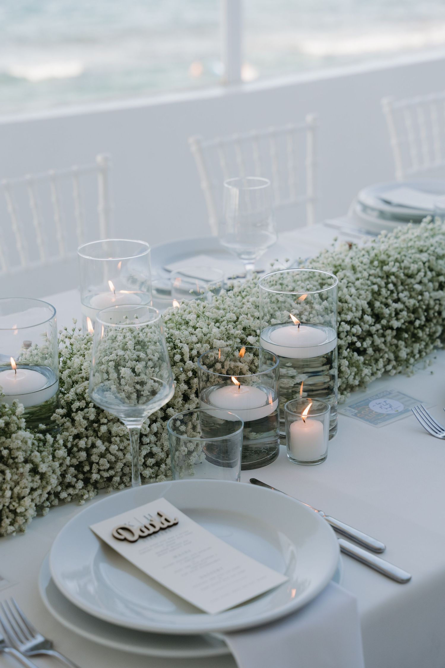 Elegant wedding table setting with white baby's breath garland centerpiece and floating candles in glass holders.