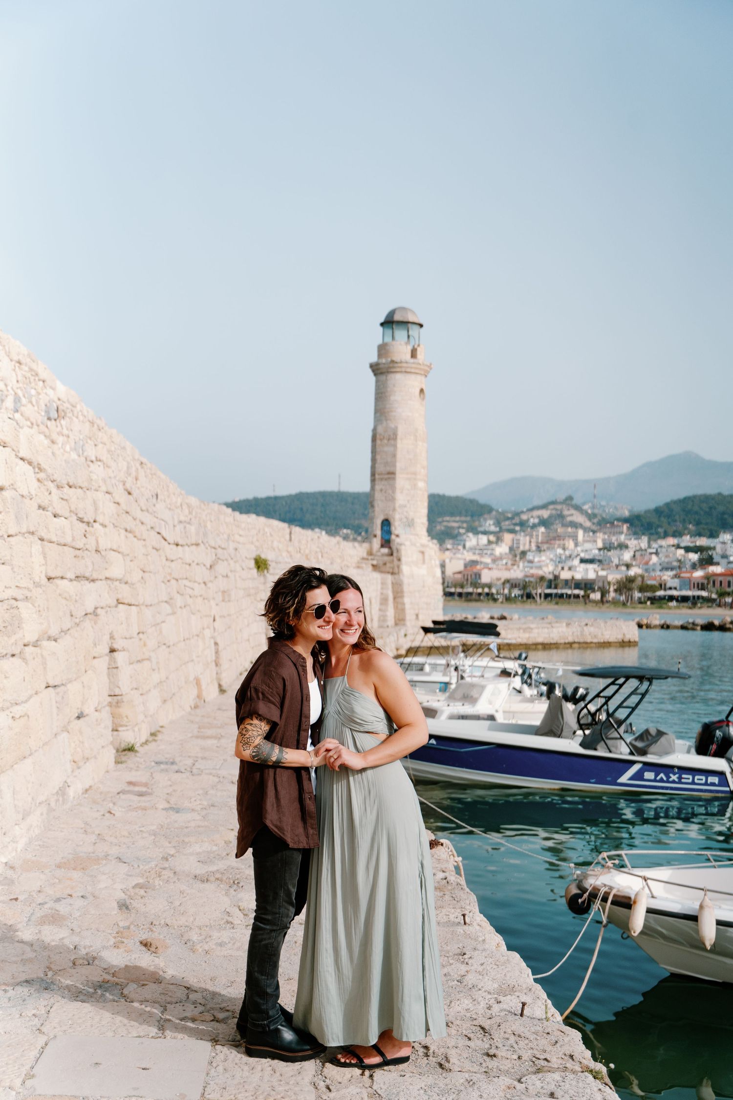 Scenic harbor view showing white lighthouse tower and boats docked along Mediterranean coastline in Rethymno, Crete
