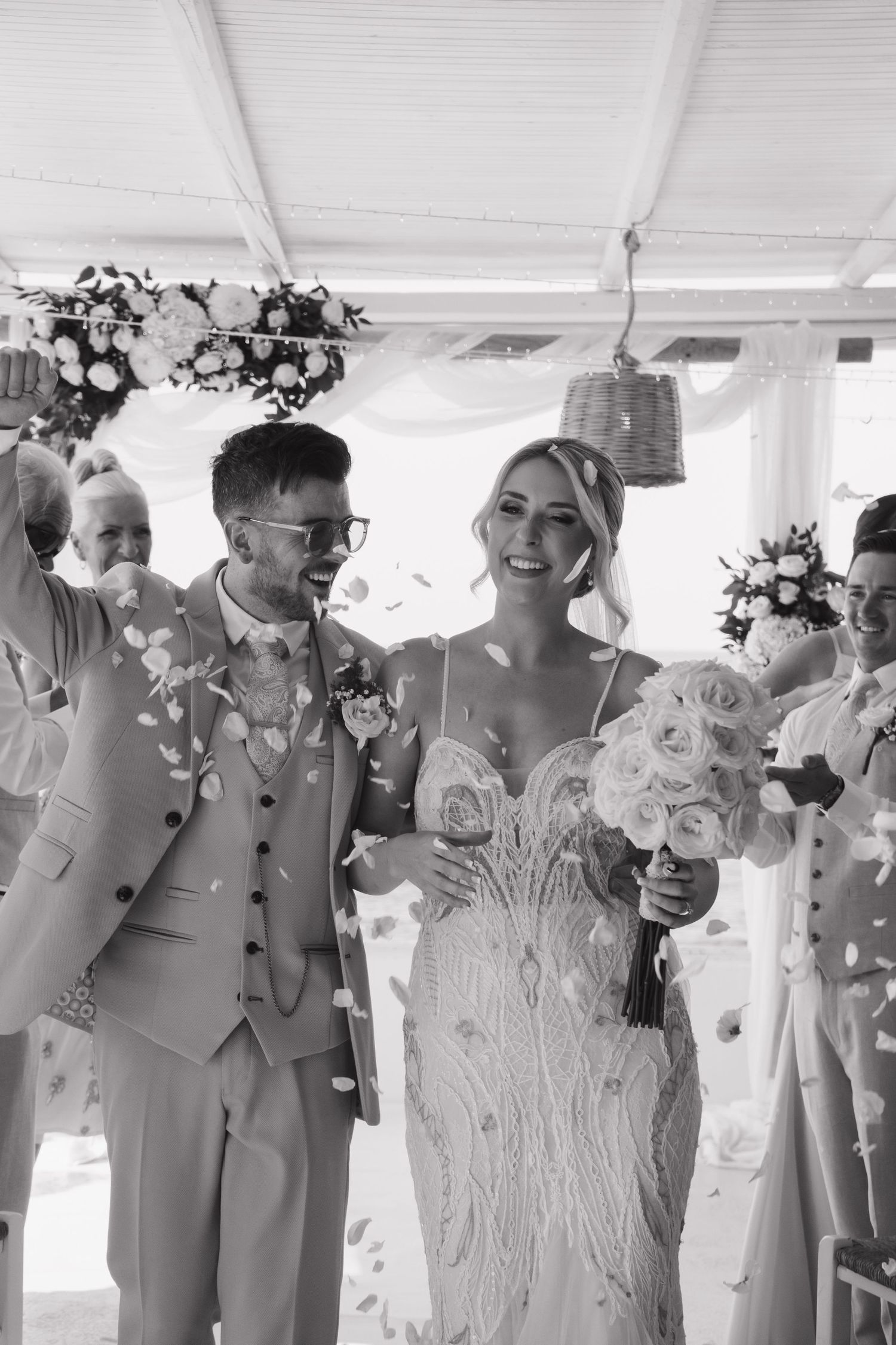 A black and white photo of a couple being showered with confetti during their wedding celebration.