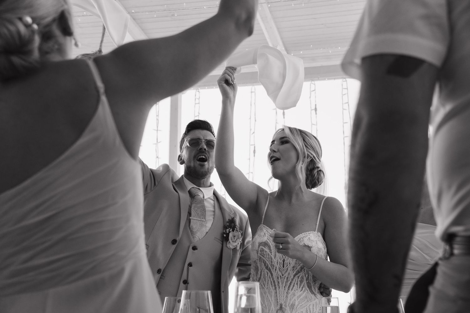 Wedding guests celebrating and dancing at a beachside reception in black and white photography.