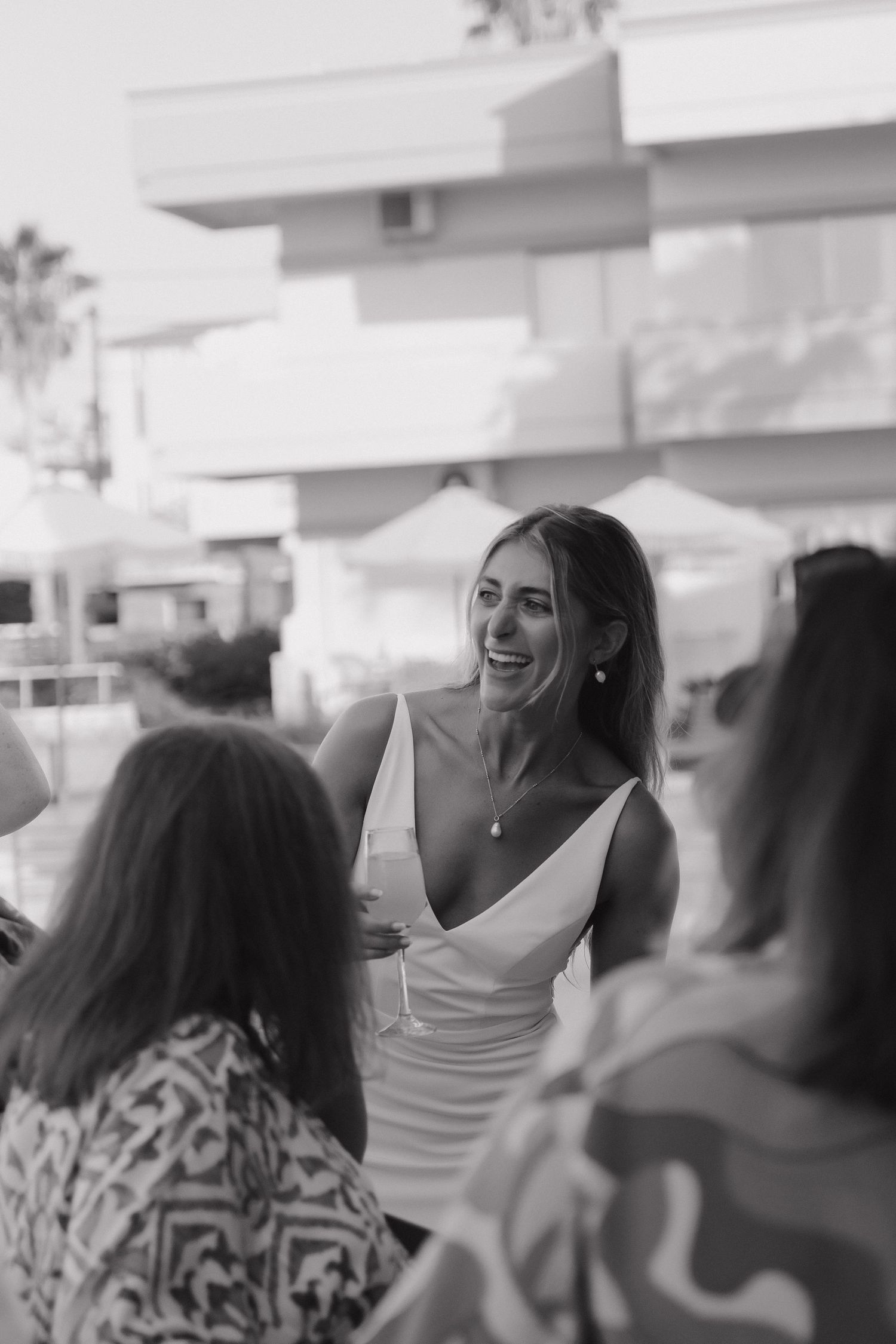 A black and white candid photo of wedding guests enjoying conversation at an outdoor venue.