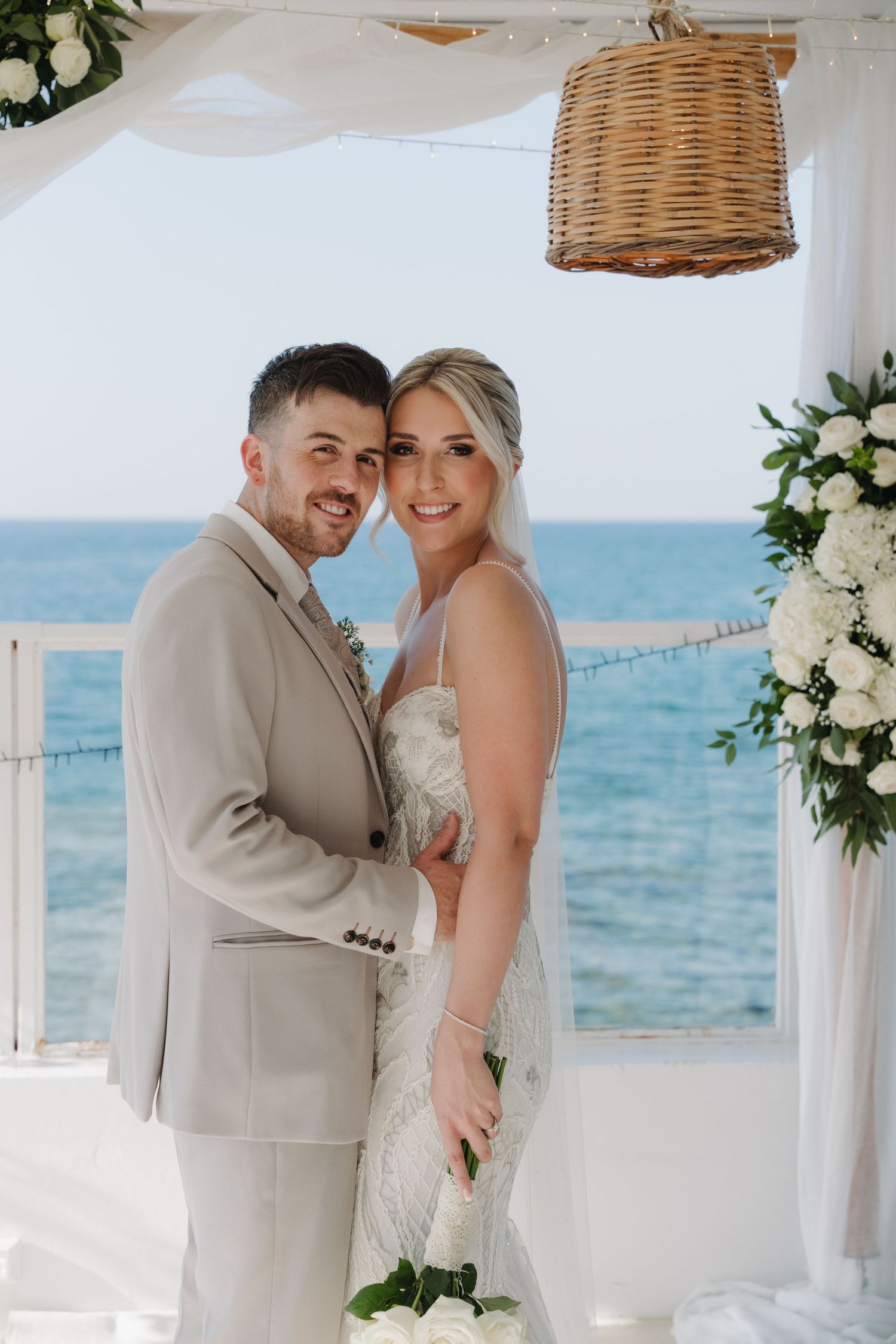 A couple shares an intimate moment at their beach wedding ceremony under a white canopy with ocean views.