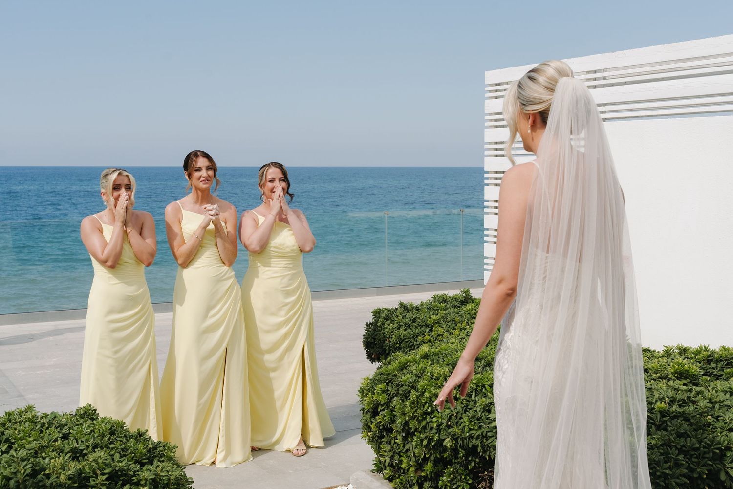 Emotional first look moment between bridesmaids and bride at oceanfront wedding venue.
