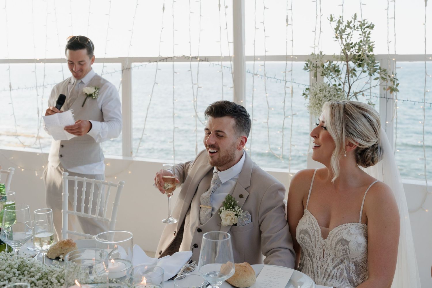 Wedding reception by the ocean with white chairs and coastal decor.