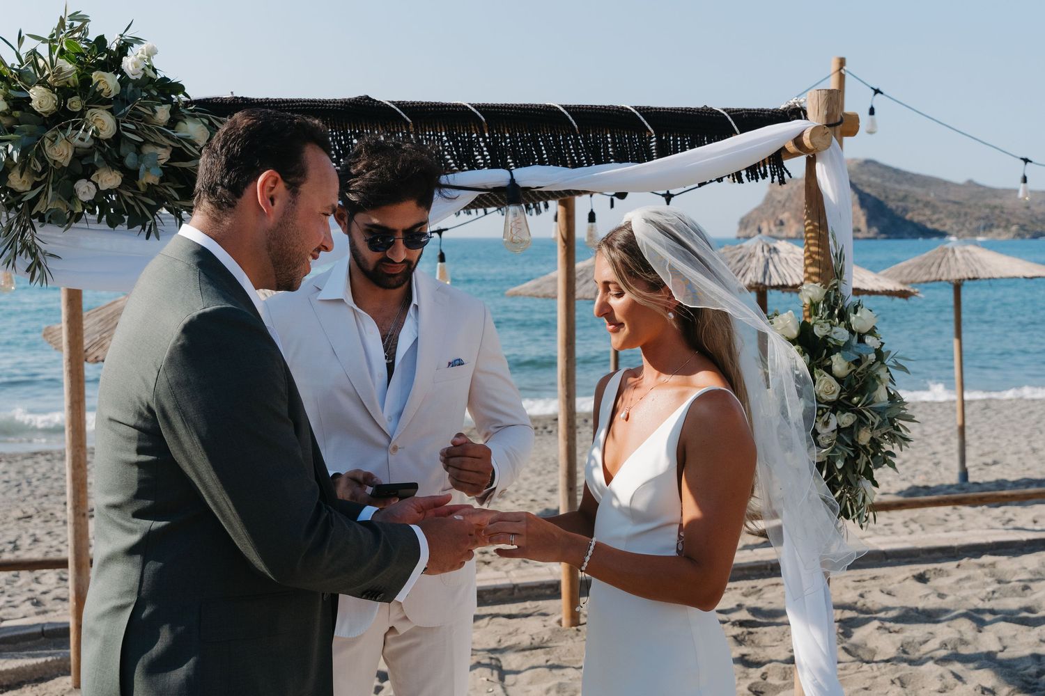 Intimate beach wedding ceremony under a floral arch with ocean backdrop.