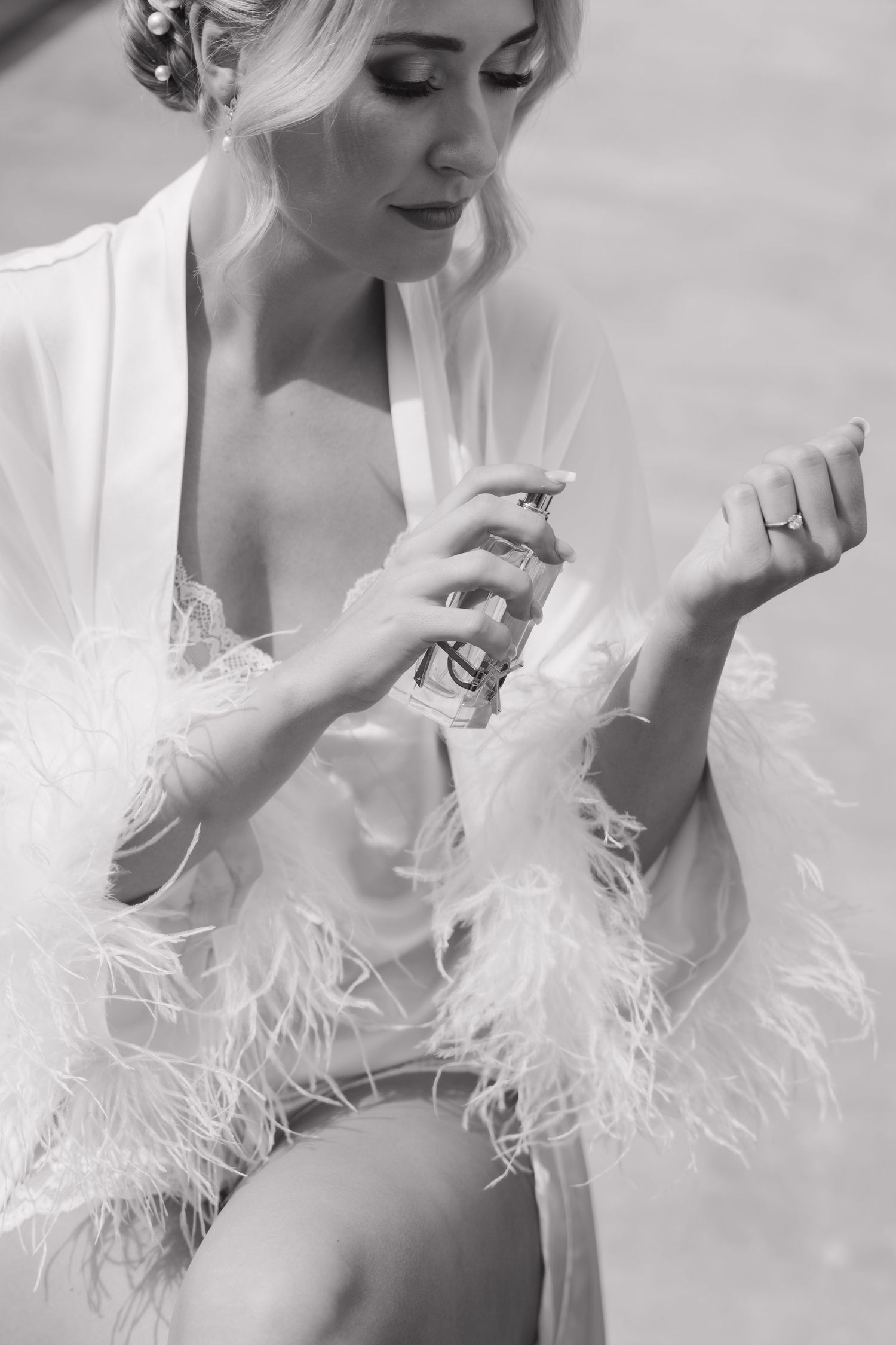 Close-up shot of perfume being applied to wrist with feathered white robe details.