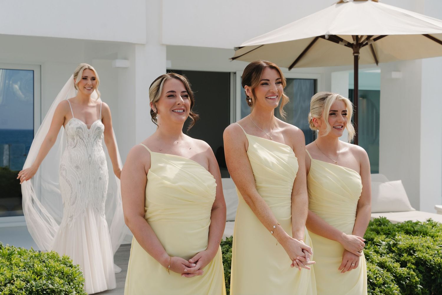 Bride and bridesmaids in yellow dresses standing under beach umbrella.