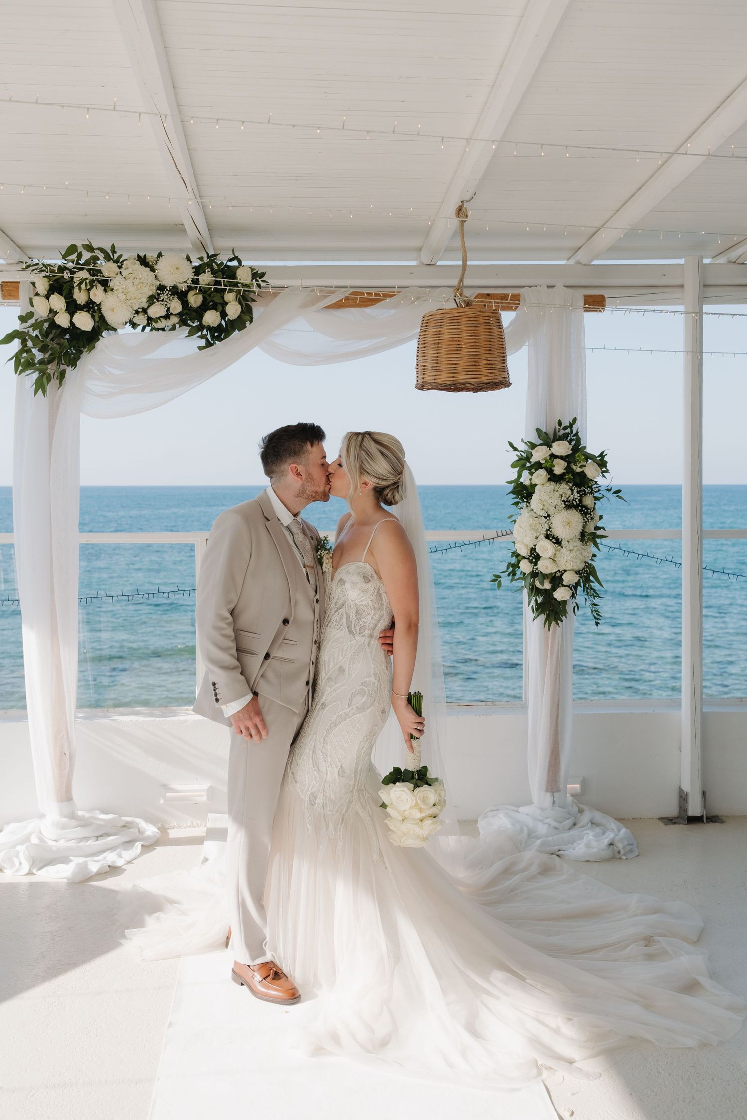 A romantic beach wedding ceremony setup with white drapes and floral arrangements overlooking the ocean.