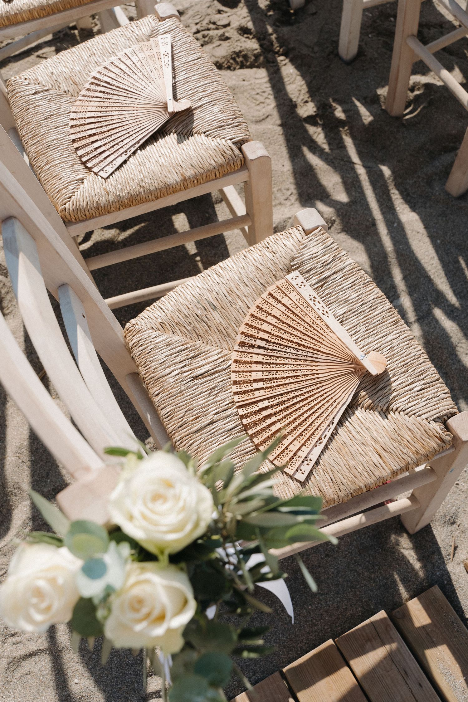 Rustic woven chairs with wooden fans and white roses creating a romantic outdoor setting.