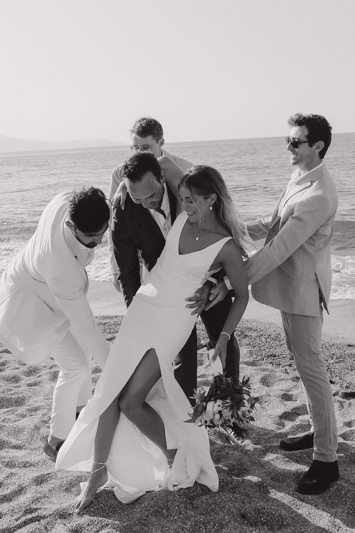 Wedding party poses playfully on a beach with white attire and dramatic poses.