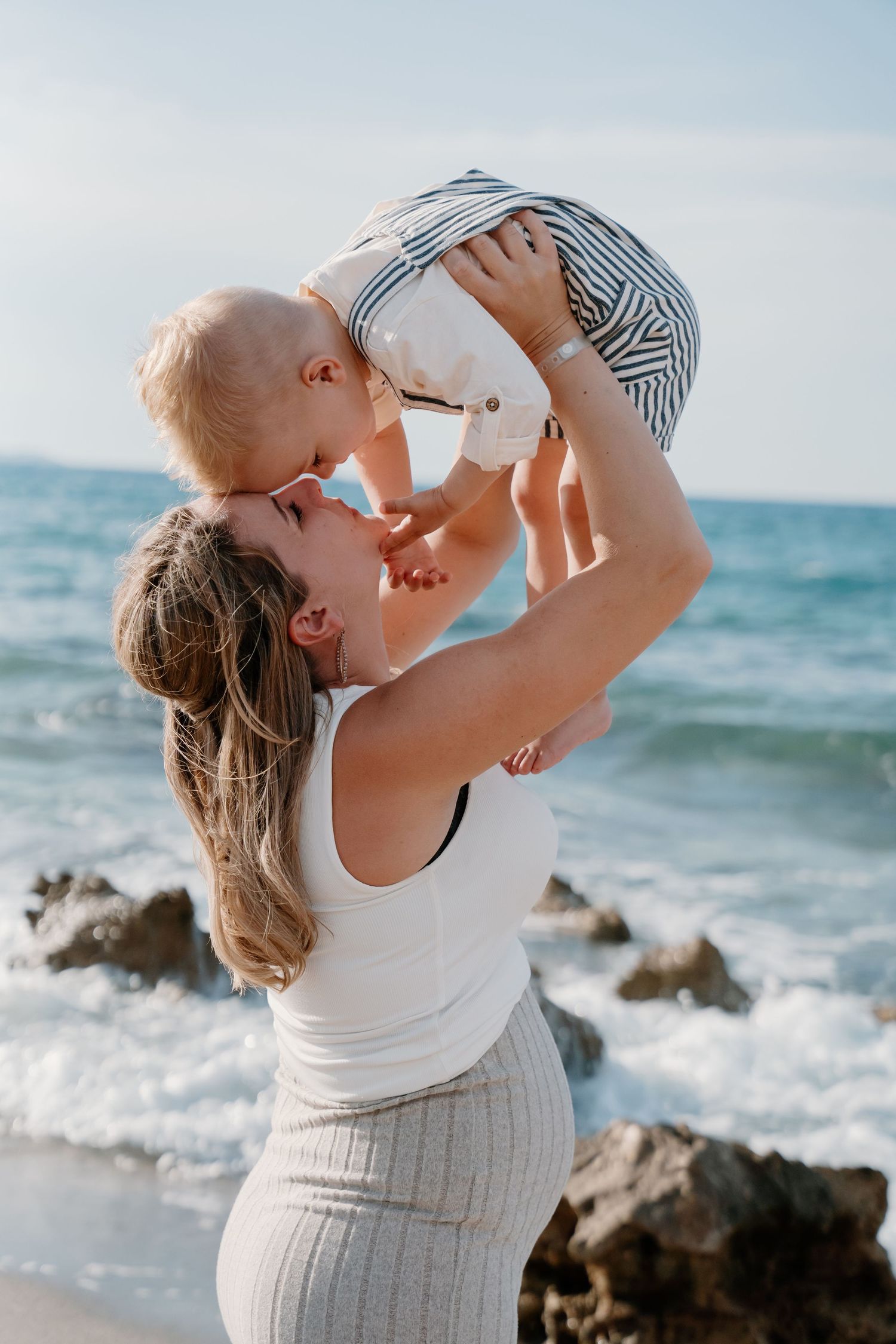 Parent lifting child playfully against blue ocean backdrop.